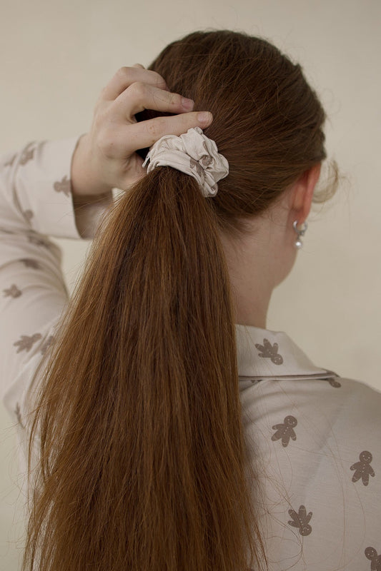 A person with a long ponytail secured by a Forever French Baby Scrunchie | Gingersnap, a bamboo scrunchie featuring a gingerbread man print.