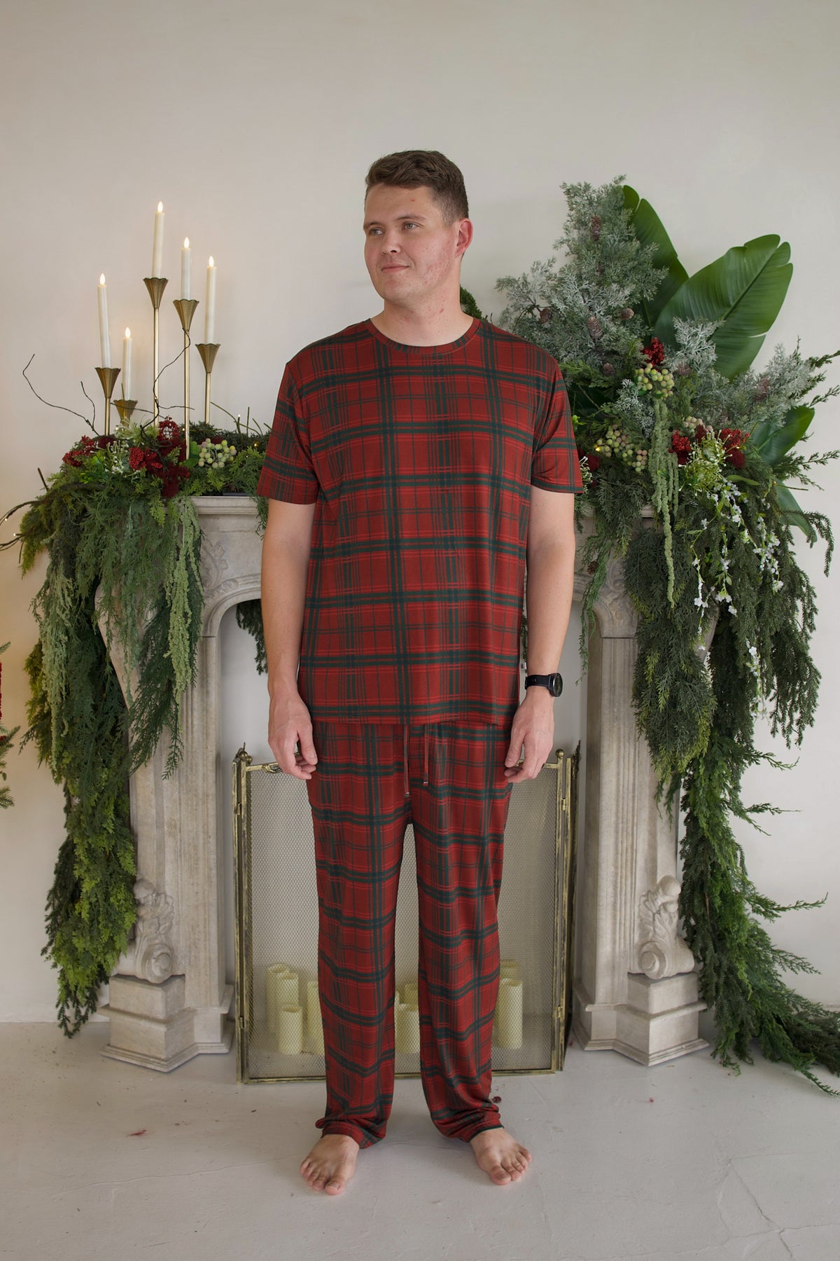 A man wearing a red and green Christmas Plaid Men’s Short Sleeve Pajamas set consisting of a short-sleeve bamboo shirt and pants.