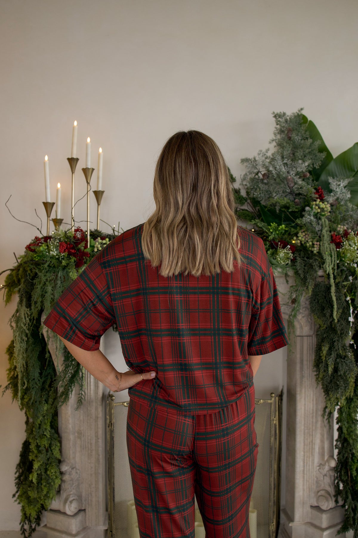 A person seen from behind wears the Women’s Boxy Tee Lounge Set in Christmas Plaid, featuring a short-sleeved top and pants in red and green.