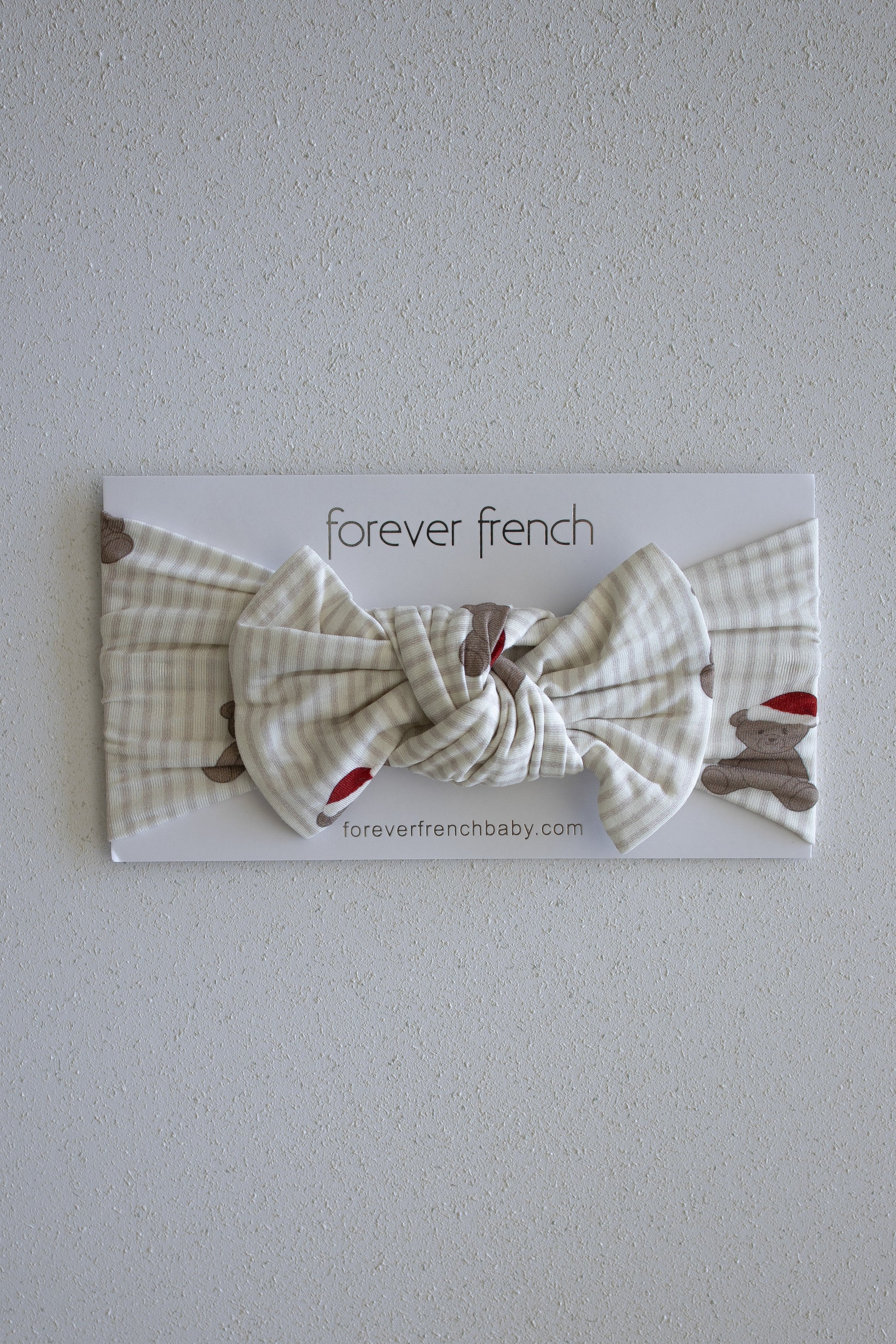 A cream and beige plaid Bamboo Head Wrap in the Santa Teddy style, featuring a large bow, is displayed on a "forever french baby" branded card against a light textured wall.
