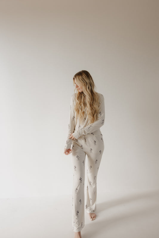 A woman with long, wavy blonde hair stands barefoot against a white background, wearing forever french baby Women’s Bamboo Pajama | All Aboard!, which features a light color and subtle dark pattern. She looks left, arms relaxed.