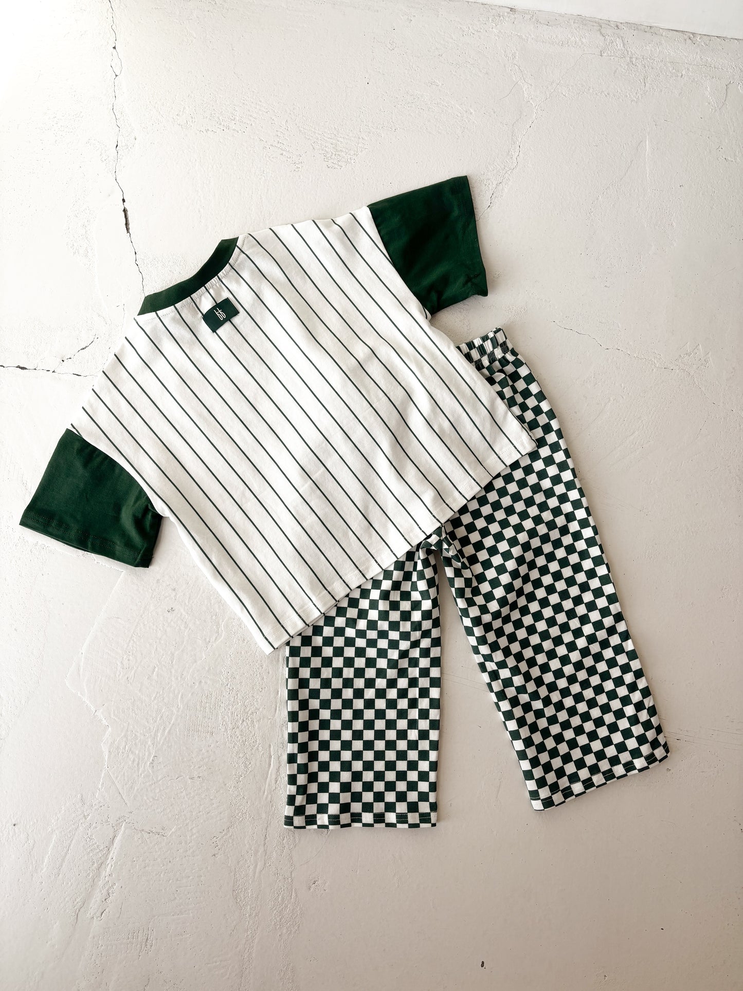 The forever french baby T-Shirt & Pant Set | Lucky Micro Check is displayed on a light surface, featuring a short-sleeve shirt with green sleeves and black pinstripes, paired with green checkerboard kids wide leg pants.
