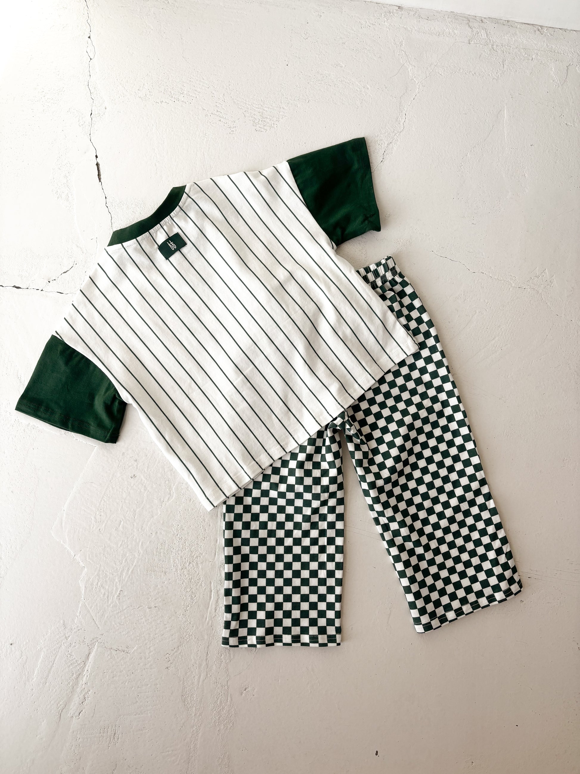 The forever french baby T-Shirt & Pant Set | Lucky Micro Check is displayed on a light surface, featuring a short-sleeve shirt with green sleeves and black pinstripes, paired with green checkerboard kids wide leg pants.
