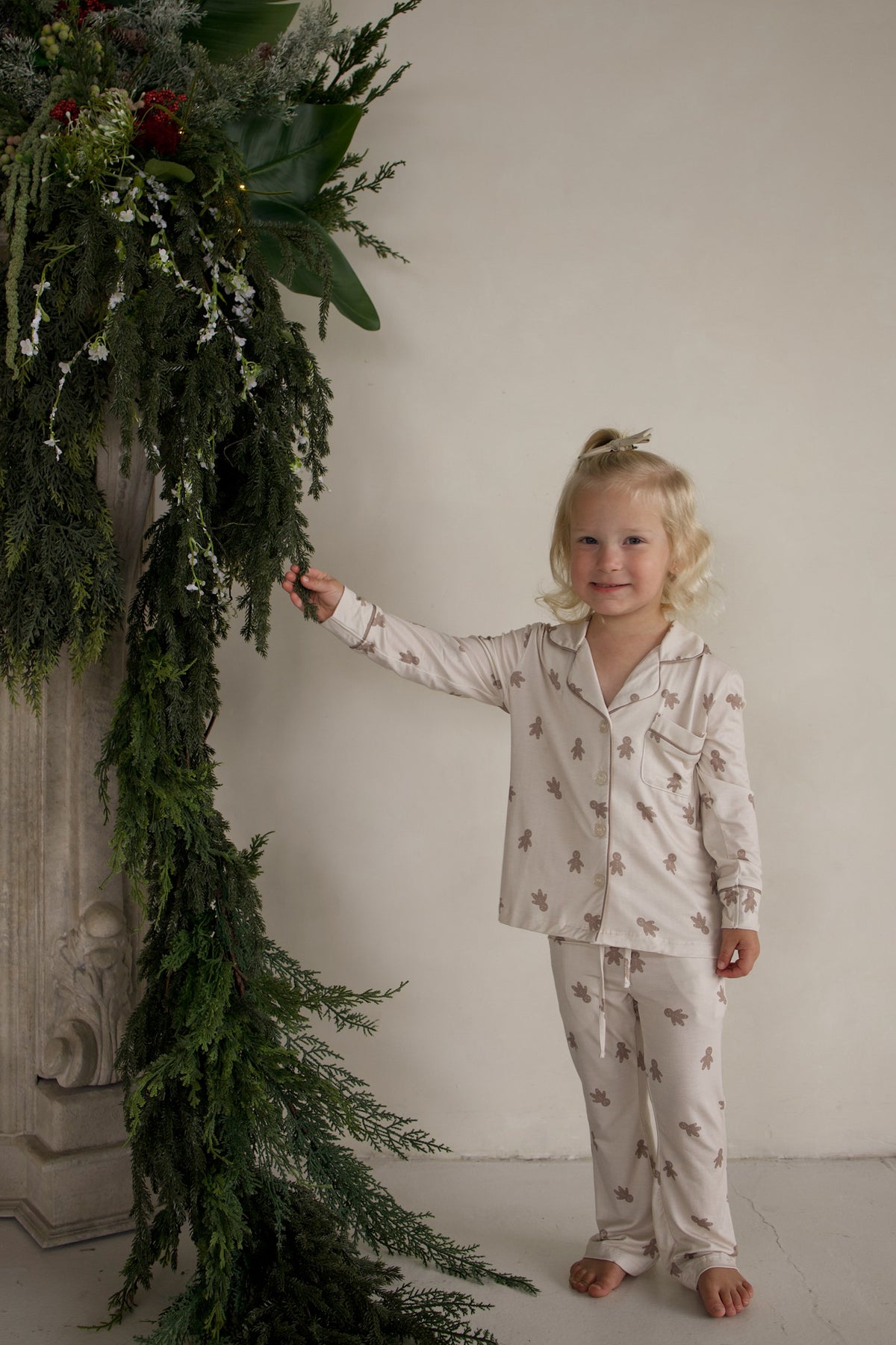 A young girl wearing a long-sleeved Girl’s Bamboo Button Up Lounge Set in the Gingersnap gingerbread man print.