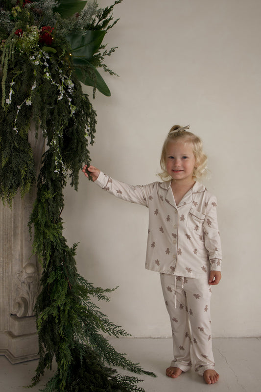 A young girl wearing a long-sleeved Girl’s Bamboo Button Up Lounge Set in the Gingersnap gingerbread man print.