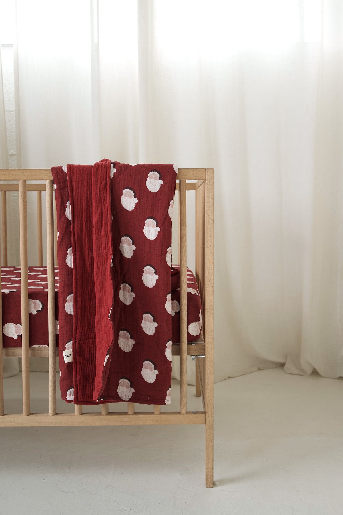 A red forever french baby Muslin Quilt | Vintage Santa draped over a wooden crib.