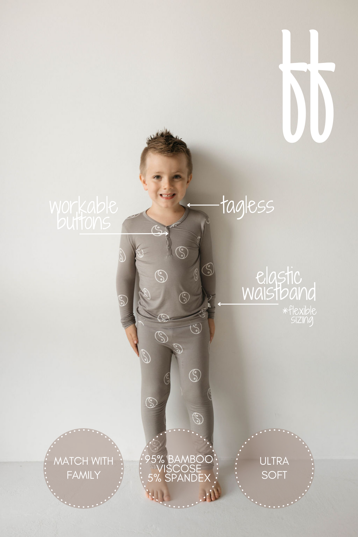 A child wearing forever french baby's Bamboo Two Piece Pajamas in Sage Yin Yang stands against a grey background. These hypo-allergenic pajamas, featuring an elastic waistband, workable buttons, and a tagless design, showcase a light grey color with circular patterns. Text highlights the material composition (95% bamboo viscose and 5% spandex) and the ultra-soft, breathable fabric. Other text mentions matching with family.