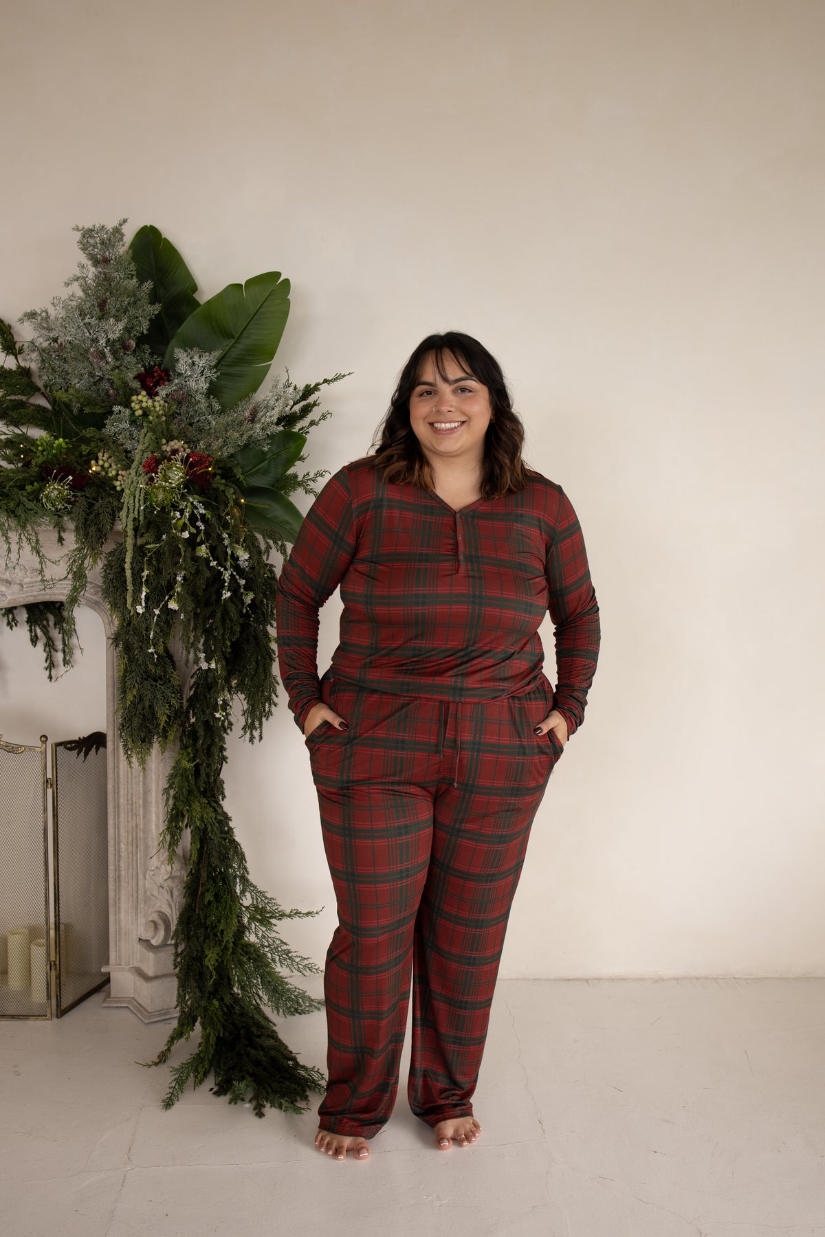 A smiling person wears a Women’s Long Sleeve Bamboo Pajama | Christmas Plaid set in red and green, featuring pants with side pockets.