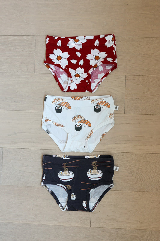 Three pairs of hypoallergenic Girl's Bamboo Briefs by forever french baby are laid out: Cherry Blossoms print on top, a playful Ramen & Sushi pattern in the middle, and a dark blue pair featuring sushi at the bottom.