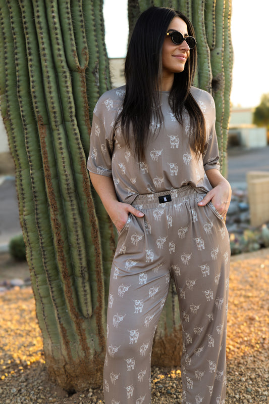 A woman wearing the forever french baby Women's Boxy Tee Lounge Set in Highland and sunglasses stands with her hands in her pockets by a large cactus outdoors on a sunny day.