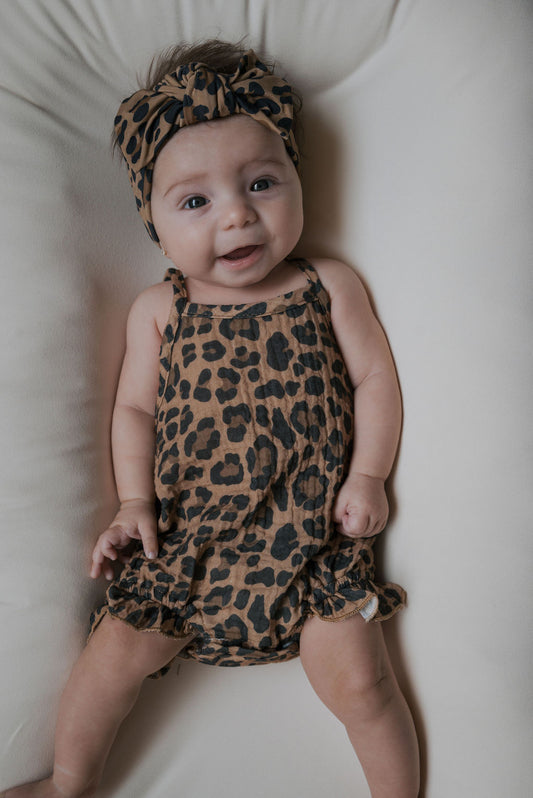 A baby smiles while wearing the forever french baby Muslin Sleeveless Tank Romper | Leopard—perfect for newborns to 24 months and ideal for showcasing trendy leopard print style.