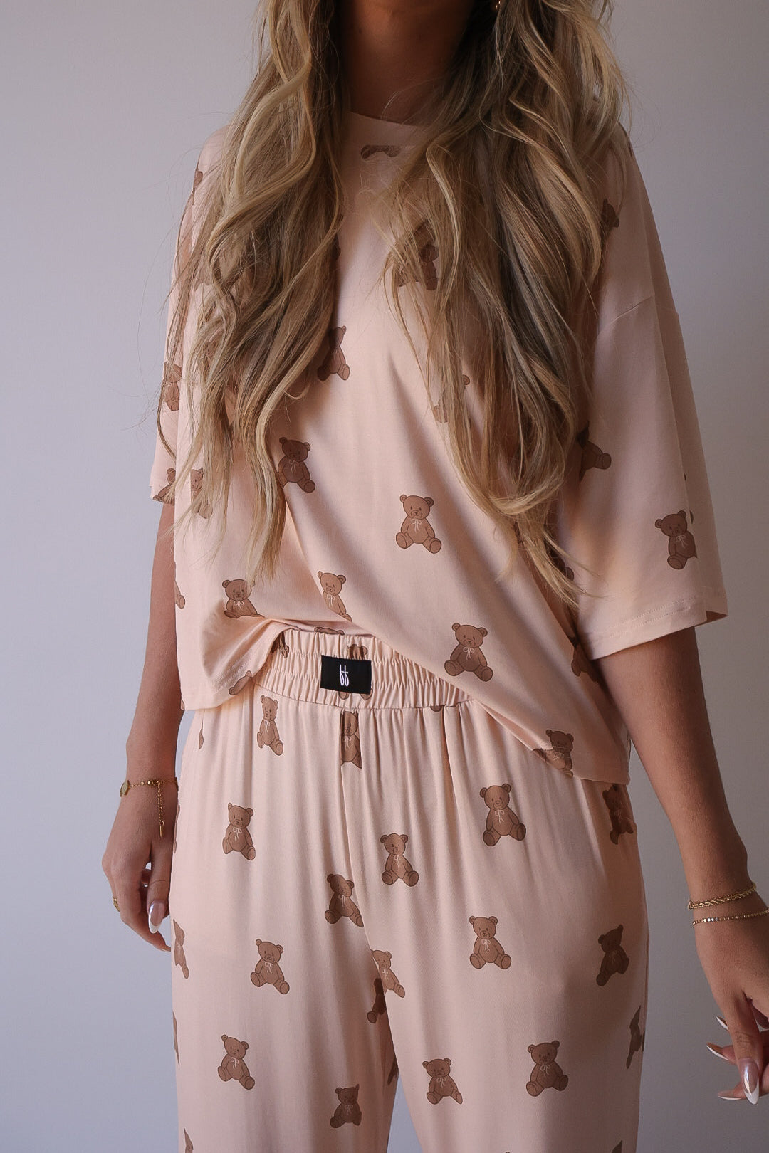 Wearing the Women's Boxy Tee Lounge Set | Lottie by forever french baby in light pink with a brown teddy bear print, this person shows off their loose wavy hair while their face is mostly out of frame. The hypo-allergenic set features a loose top and elastic waist pants.