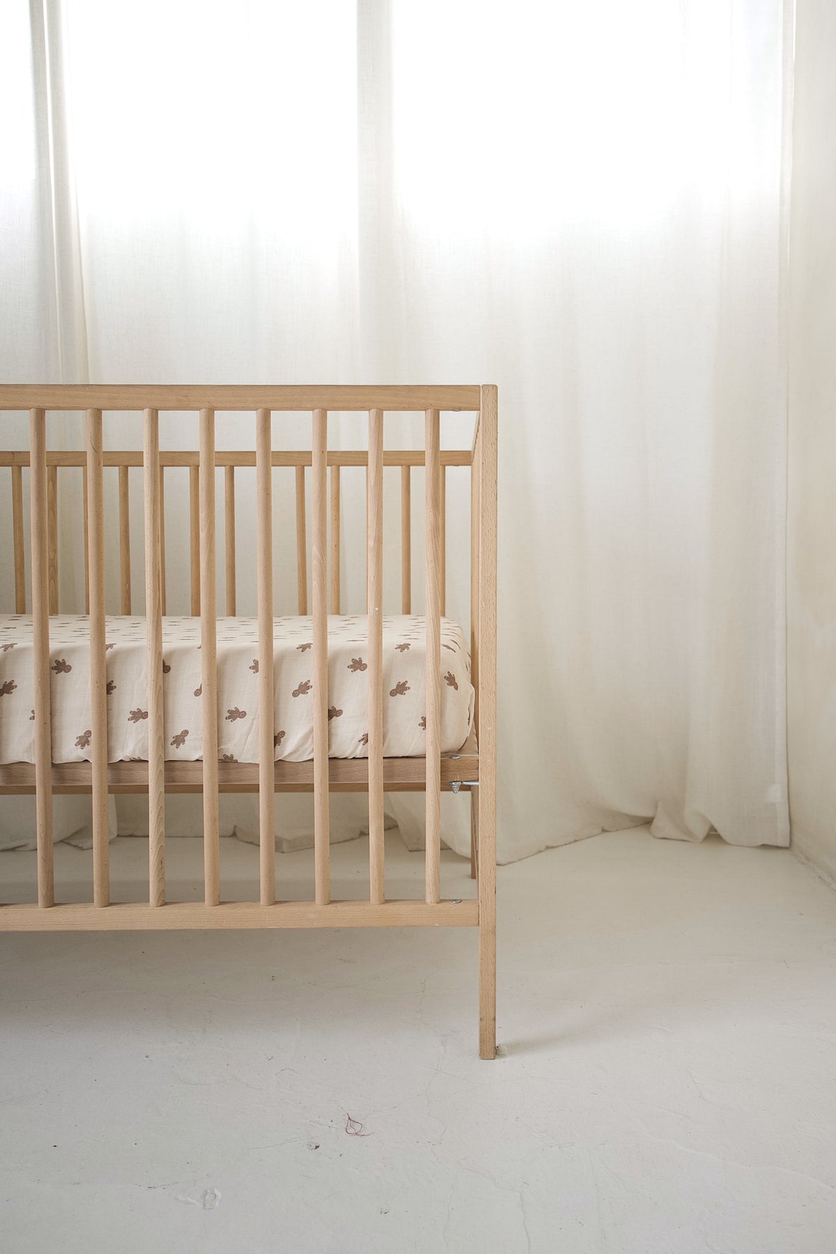 Light wood crib featuring a forever french baby Muslin Crib Sheet | Gingersnap in cream-colored muslin cotton with a brown gingerbread man pattern.
