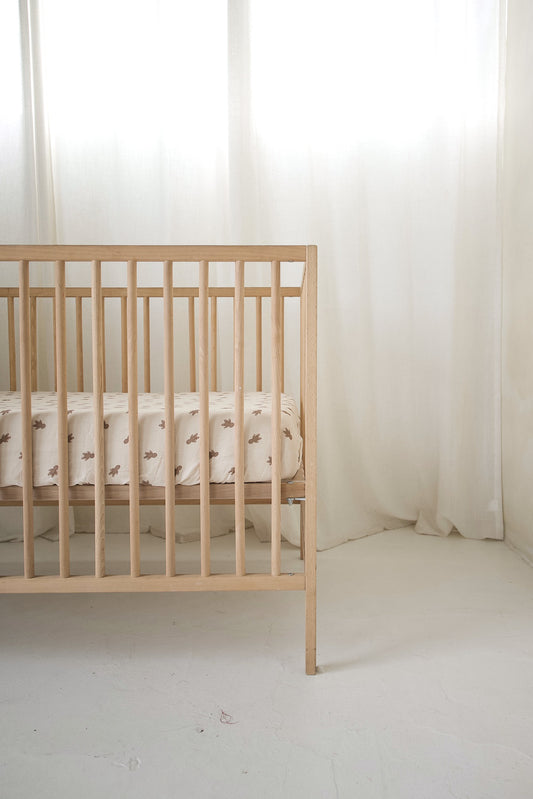 Light wood crib featuring a forever french baby Muslin Crib Sheet | Gingersnap in cream-colored muslin cotton with a brown gingerbread man pattern.