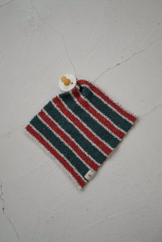 A square, textured *PRE-ORDER* Lovey | Holiday Stripe with red, green, and white holiday stripes, topped with a white pacifier.
