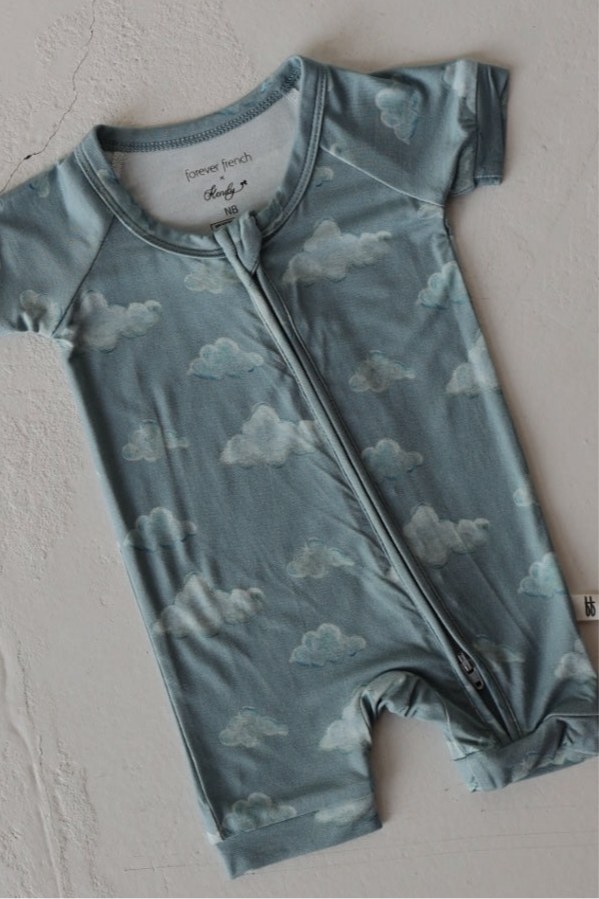 The Kendy 3 Bamboo Zip Shortie | Duke is a breathable, blue baby romper with short sleeves, a cloud pattern, and a front zipper, shown laid flat on a light surface.