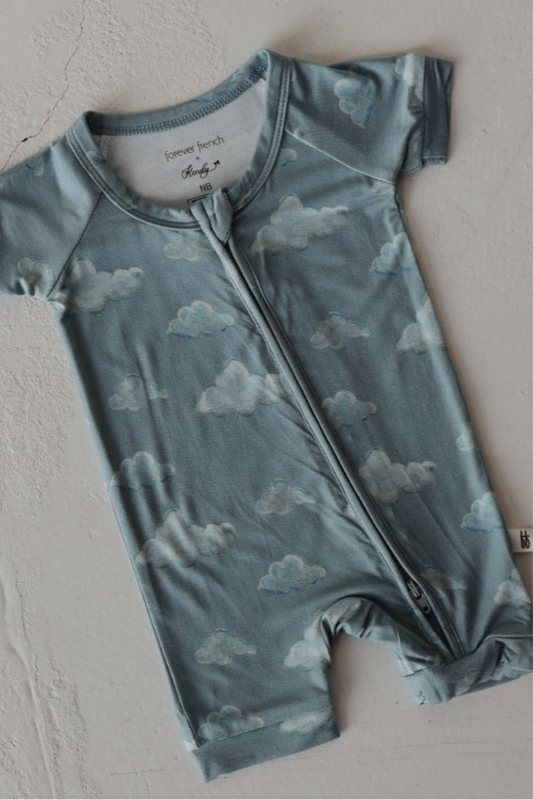 The Kendy 3 Bamboo Zip Shortie | Duke is a breathable, blue baby romper with short sleeves, a cloud pattern, and a front zipper, shown laid flat on a light surface.