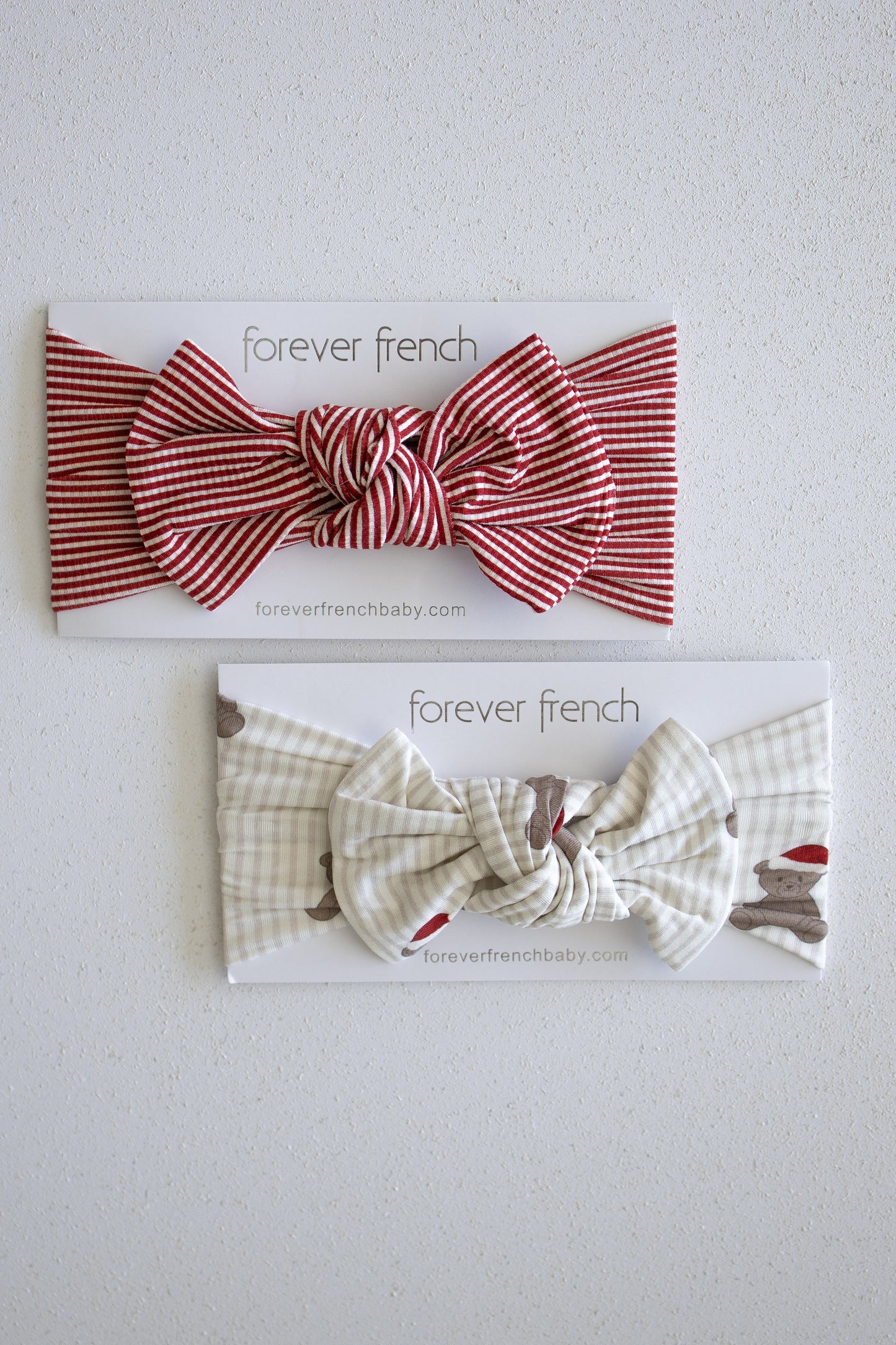 Two fabric baby headbands from forever french baby, including the Bamboo Head Wrap | Santa Teddy in cream with a bunny pattern and another in red with white stripes, each displayed on a white "forever french" branded card against a light textured background.