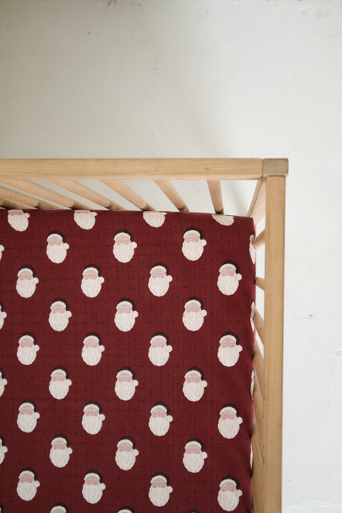 Muslin Crib Sheet | Vintage Santa featuring a repeating pattern of Santa Claus faces on a dark red background.
