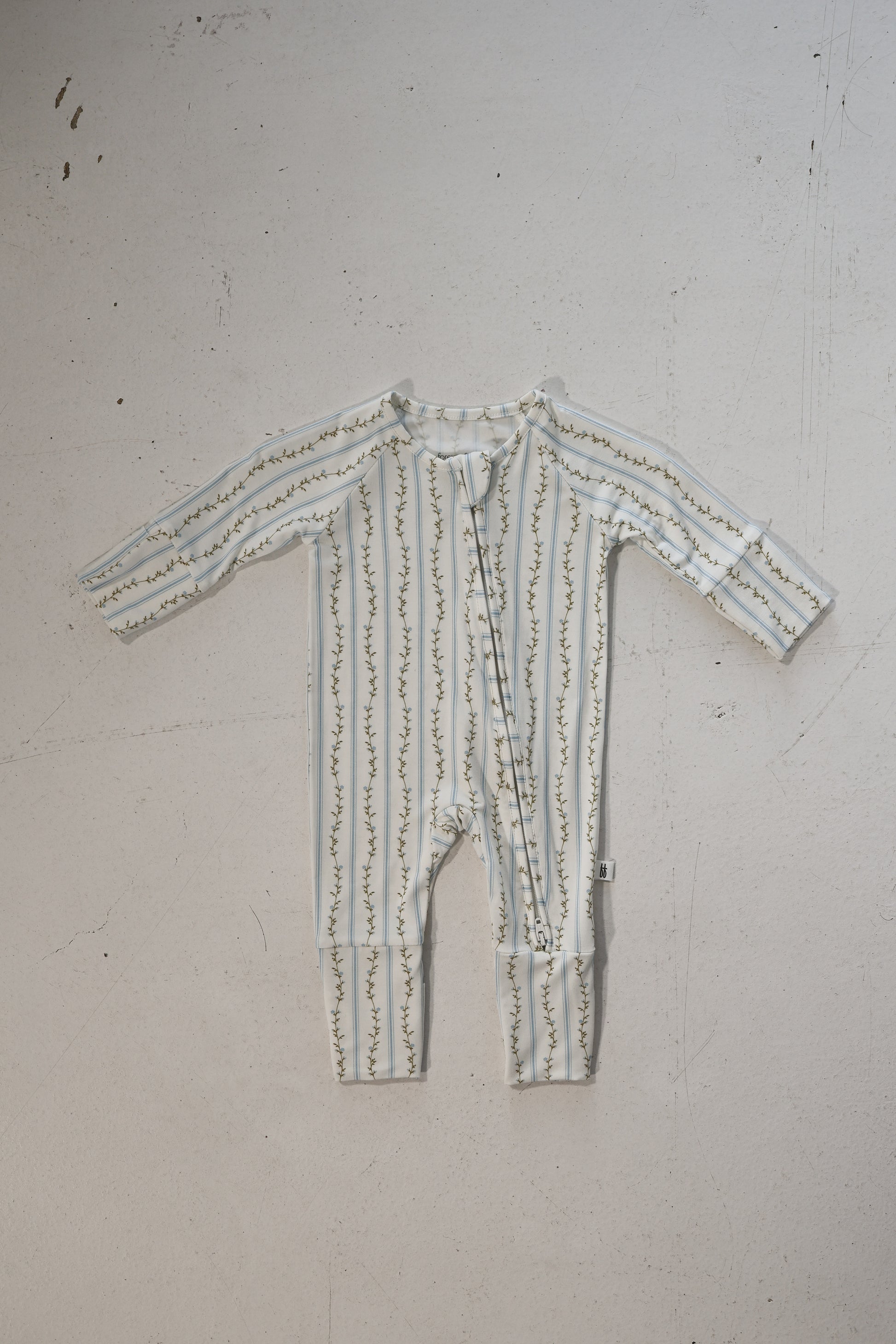 The forever french baby Bamboo Zip Pajamas | Dainty Vines features full-length, long sleeves, soft bamboo fabric, a white base with green leafy vine print, and a front diagonal zipper, shown laid flat on a light surface.
