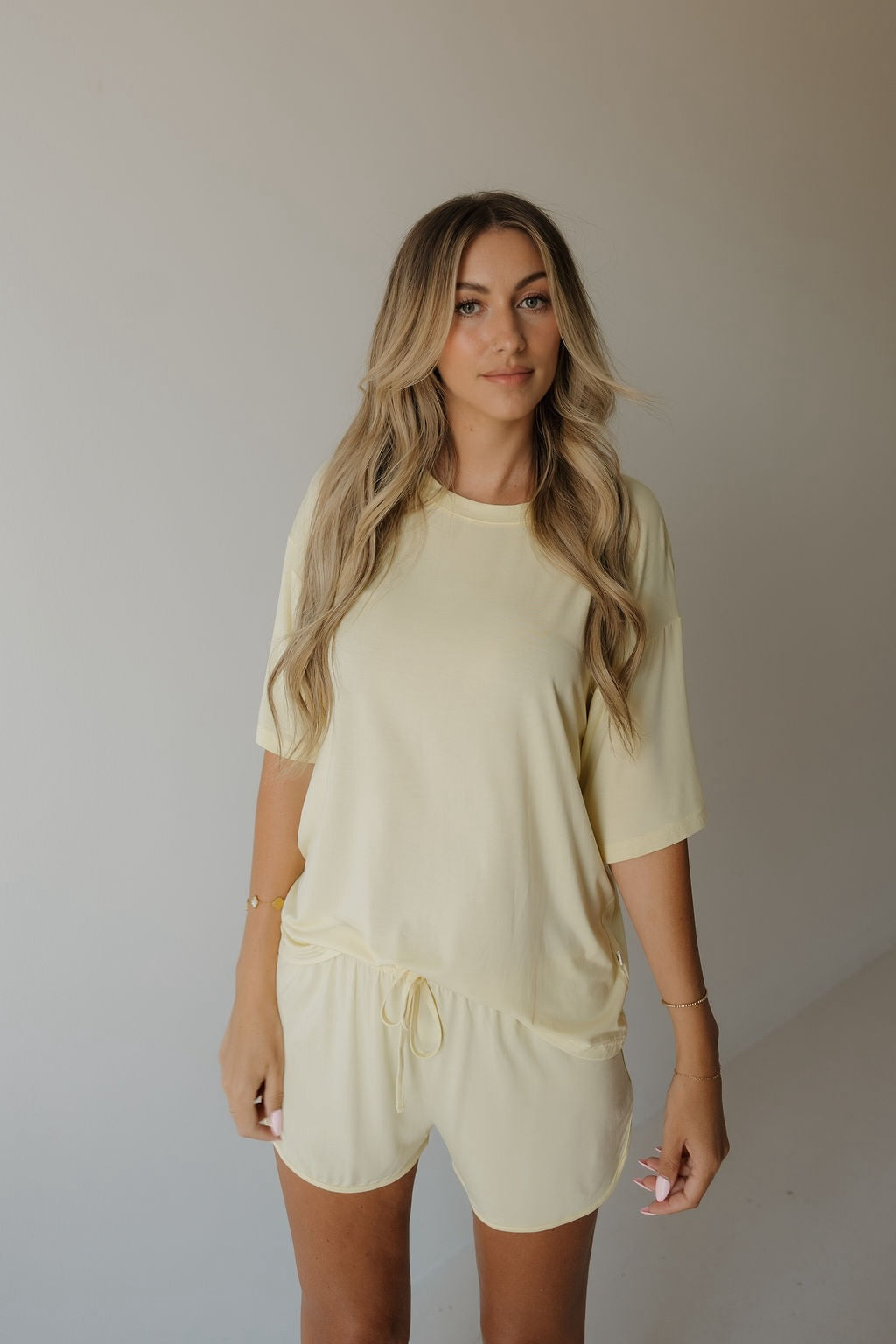 A woman with long blonde hair stands against a plain, light background, looking at the camera while wearing the forever french baby Women’s Bamboo Short Set | Sunny.