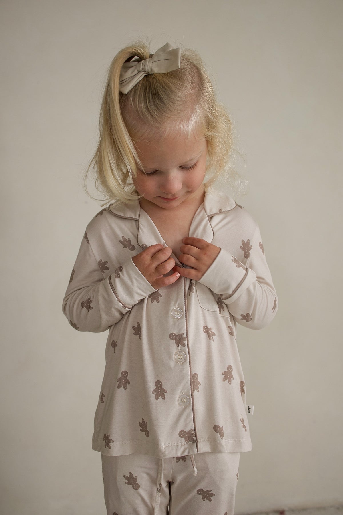 A young girl wears a long-sleeved, button-up Girl’s Bamboo Button Up Lounge Set | Gingersnap patterned with gingerbread men.