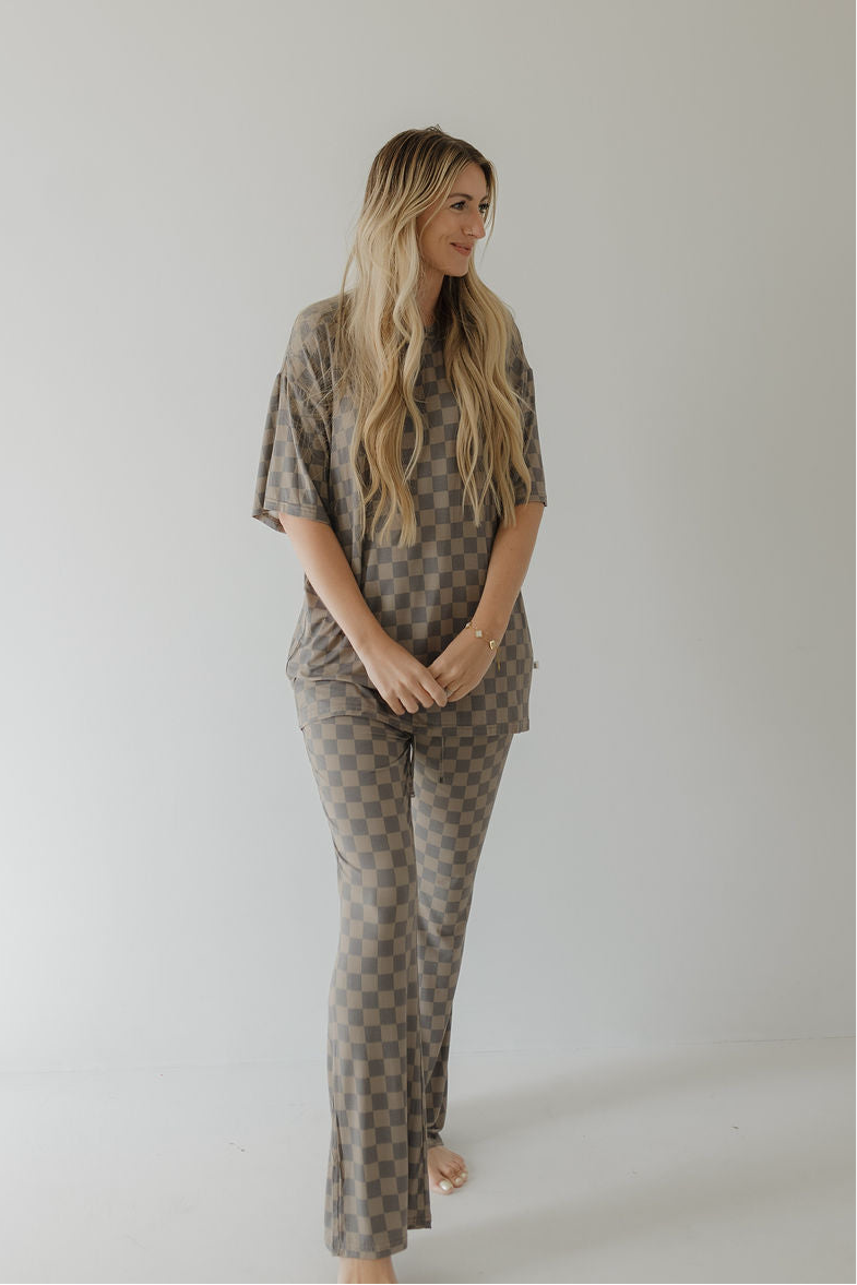 A barefoot woman with long blonde hair wears the forever french baby Short Sleeve Women's Bamboo Pajama in Faded Checkerboard, a stylish, hypo-allergenic set perfect for minimalist spaces.