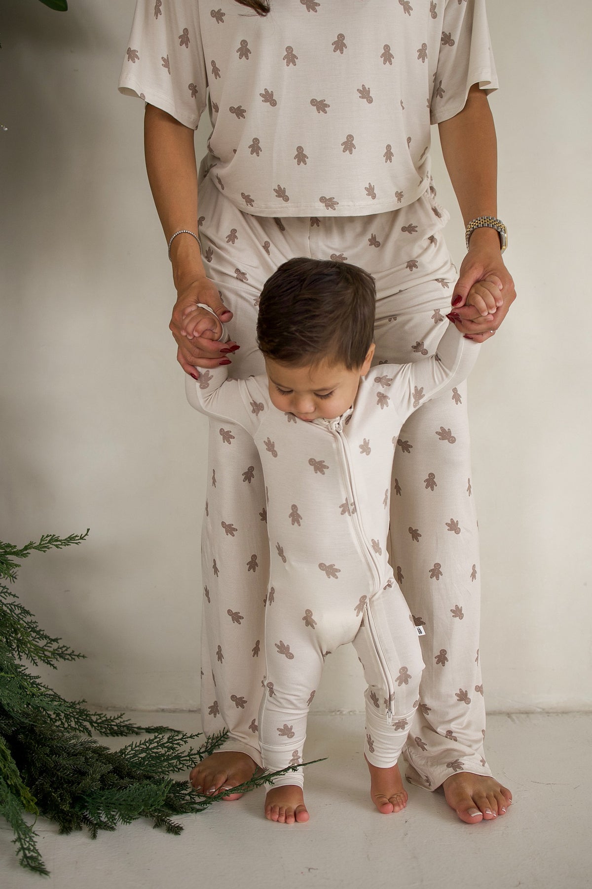 An adult wearing matching gingerbread-print pajamas holds a toddler dressed in Bamboo Zip Pajamas | Gingersnap.