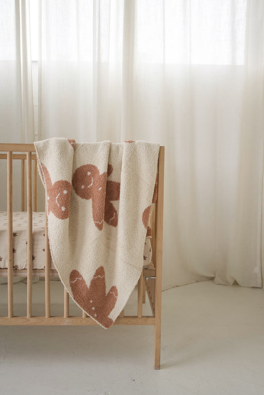 Forever French Baby *PRE-ORDER* Plush Blanket | Gingersnap in cream featuring a brown gingerbread man pattern, draped over a wooden crib.