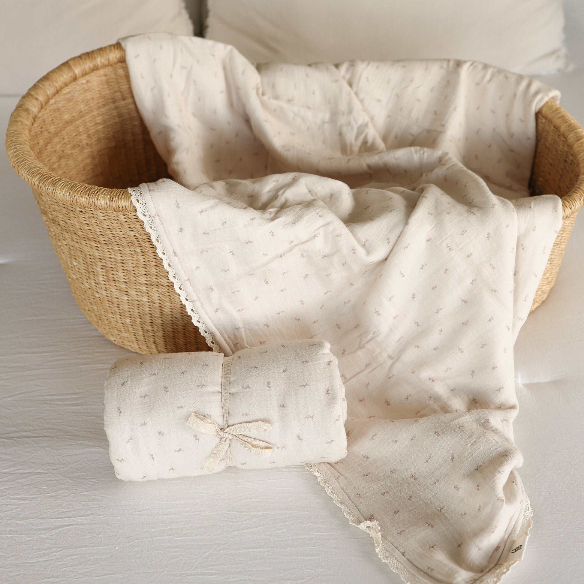 The Muslin Quilt | Lucy by forever french baby features a soft, cream-colored 100% cotton muslin quilt with a subtle pattern in a wicker basket, plus a matching rolled blanket—perfect nursery bedding for your little one.