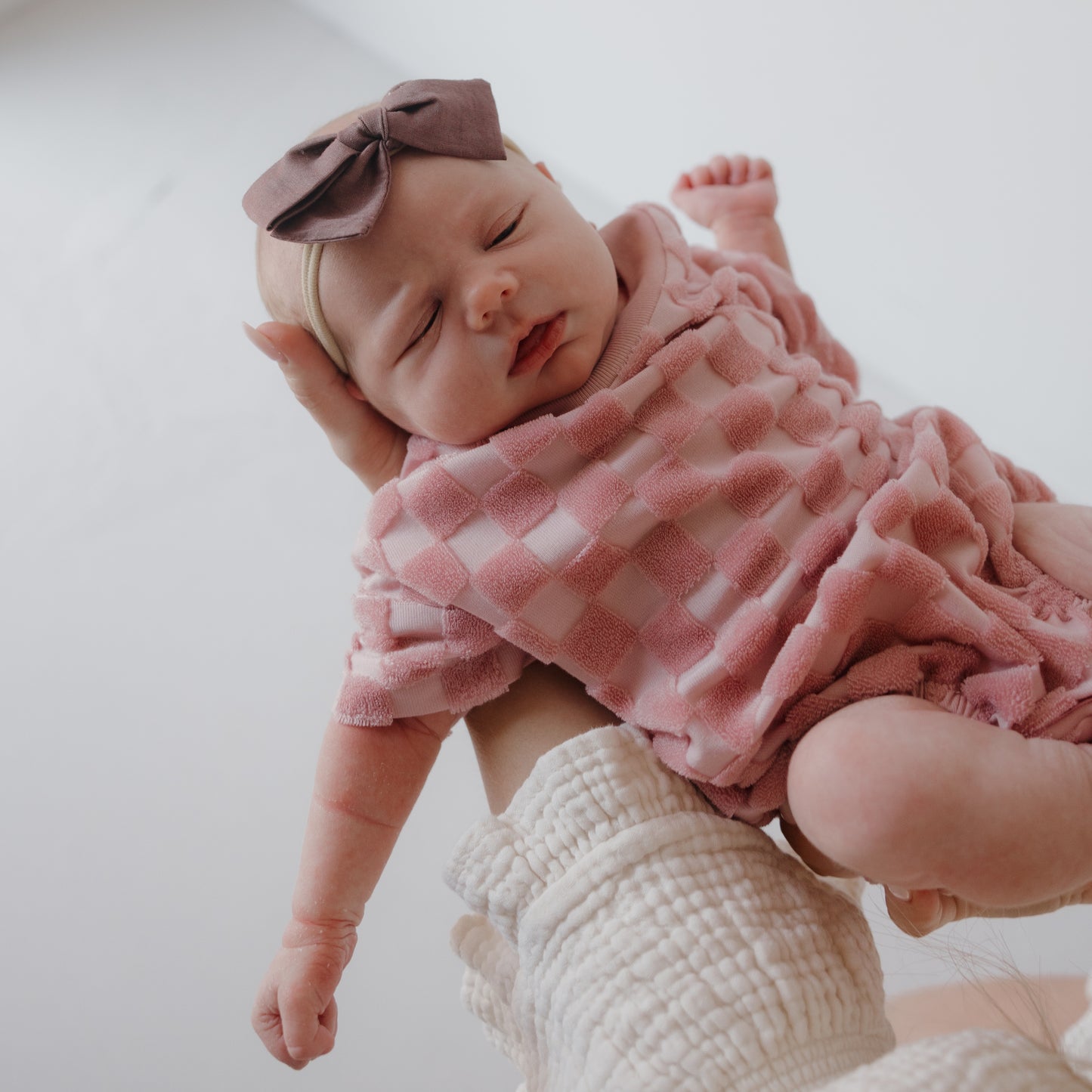 A baby in the forever french baby Terry T-Shirt Romper | Sea Pink is held by an adult, creating a sweet family matching outfits moment against a light background.