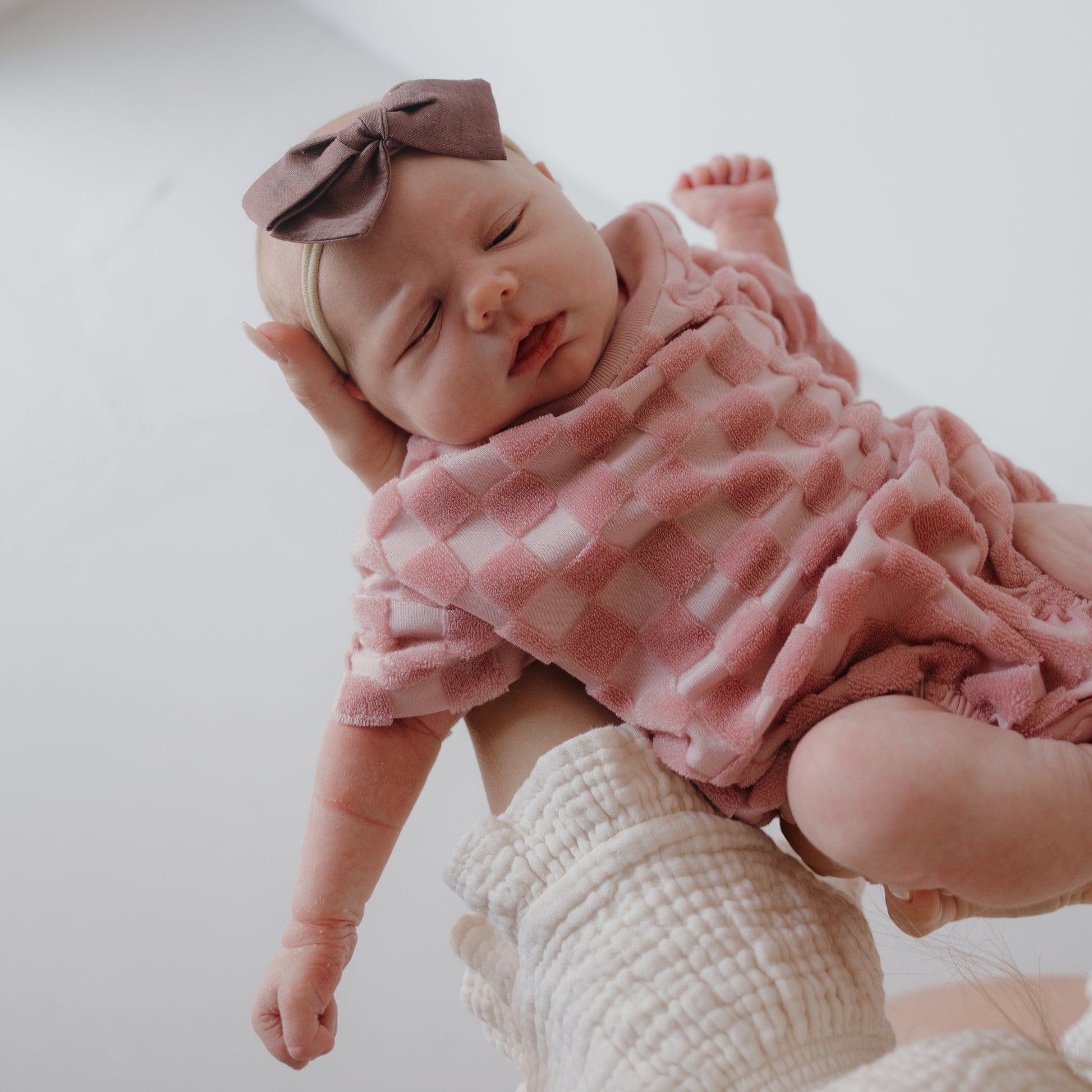 A baby in the forever french baby Terry T-Shirt Romper | Sea Pink is held by an adult, creating a sweet family matching outfits moment against a light background.