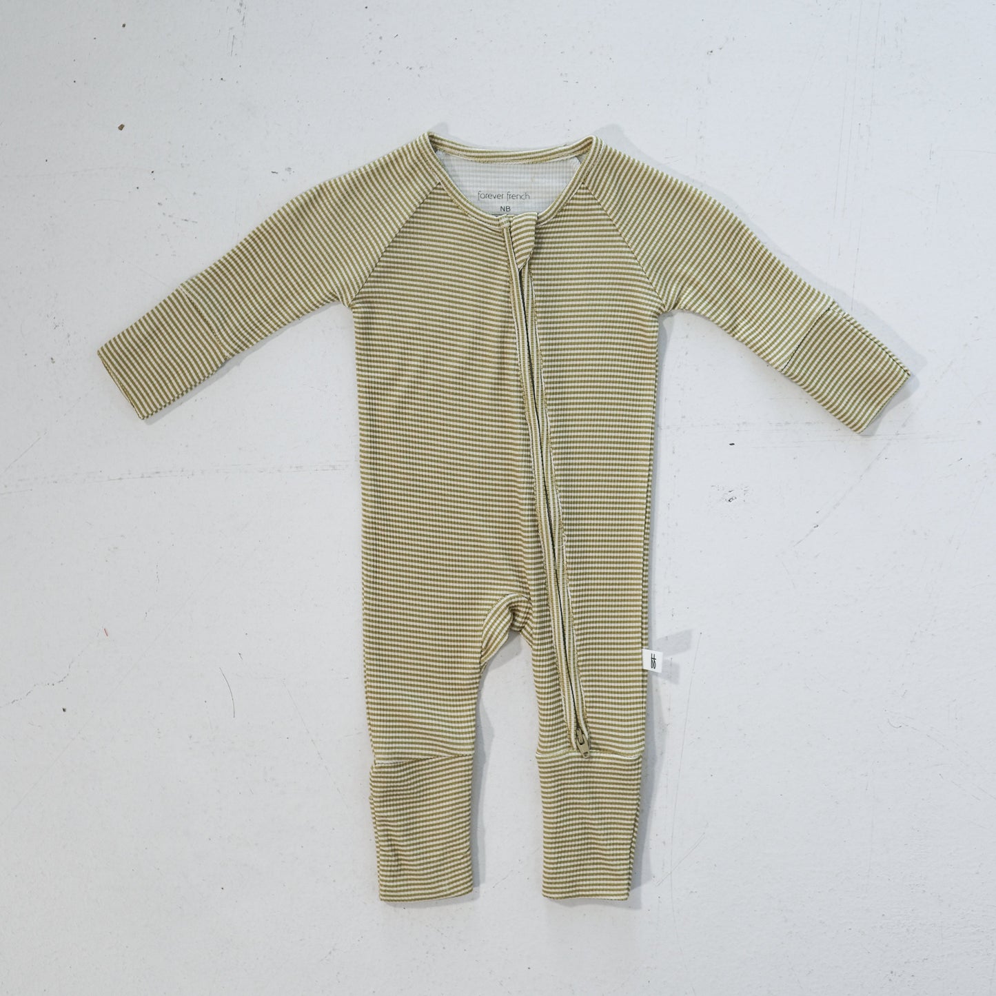 The forever french baby Bamboo Zip Pajamas in Willow Stripe Ribbed, featuring beige and white thin horizontal stripes and a diagonal zipper from neck to ankle, are laid flat on a white surface.