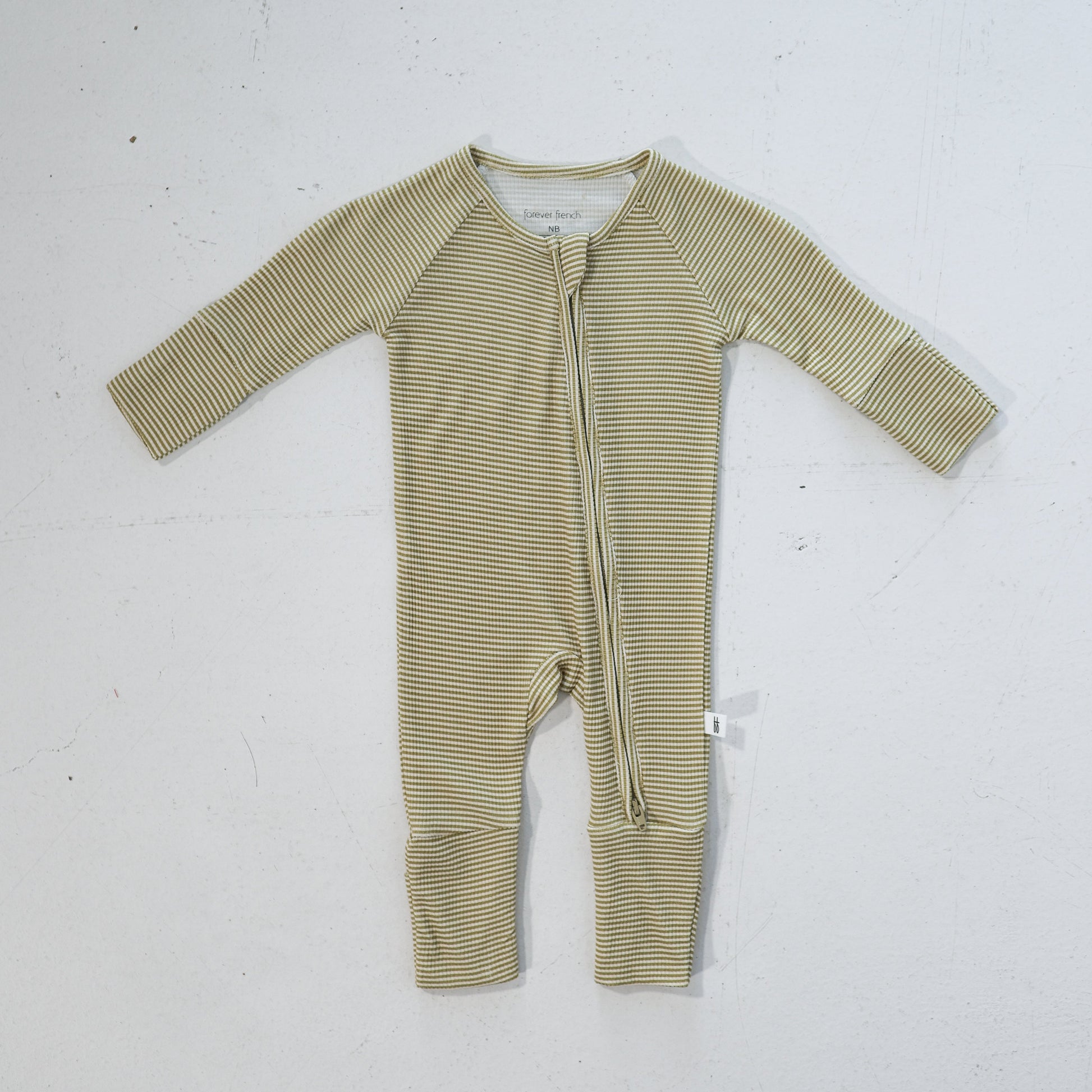 The forever french baby Bamboo Zip Pajamas in Willow Stripe Ribbed, featuring beige and white thin horizontal stripes and a diagonal zipper from neck to ankle, are laid flat on a white surface.