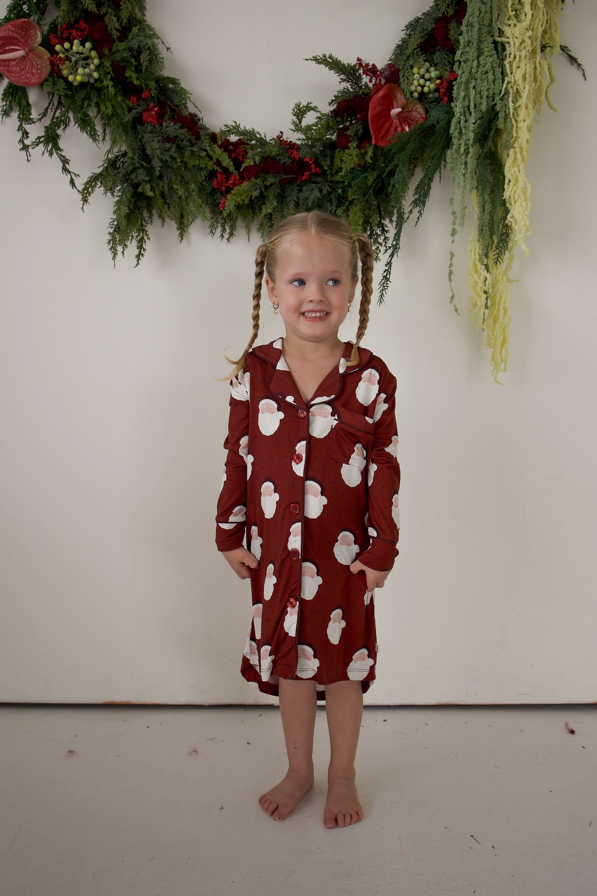 A young child wears a long-sleeved, button-down Bamboo Sleeping Dress | Vintage Santa featuring a vintage Santa Claus pattern.