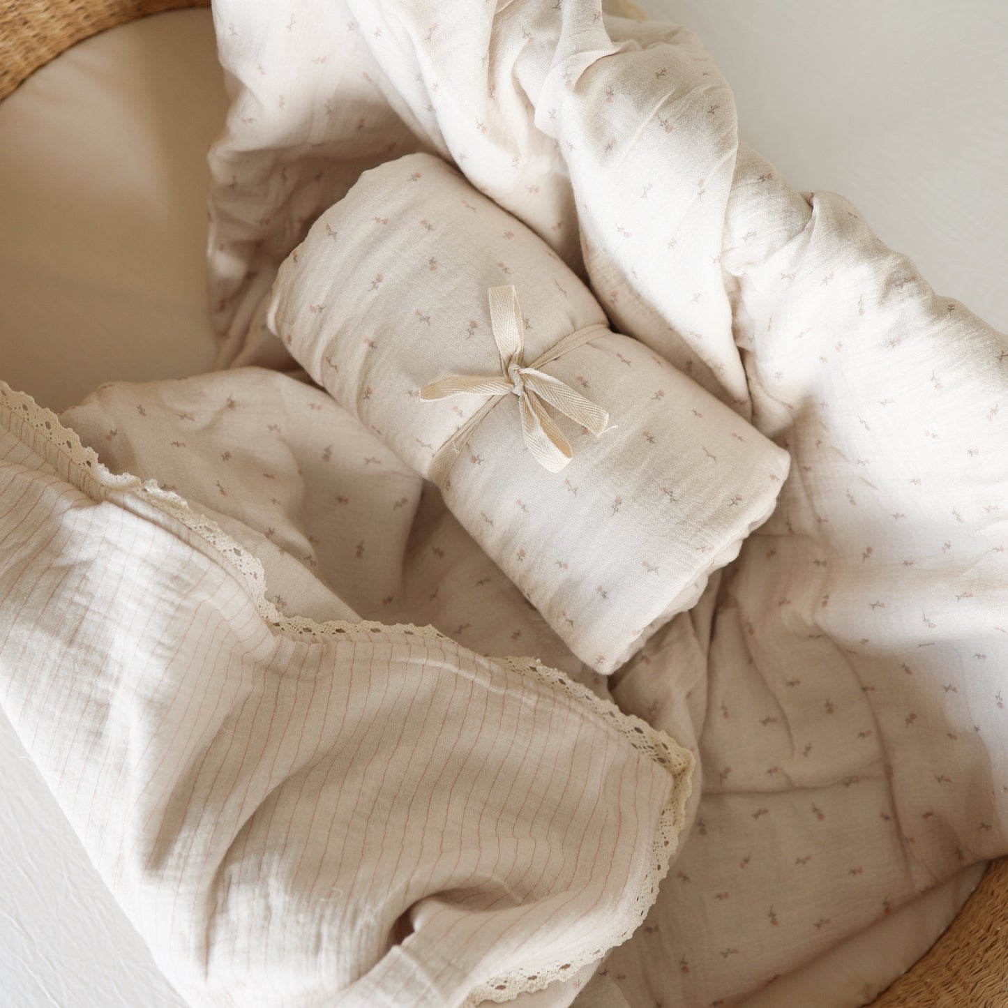 The Muslin Quilt | Lucy by forever french baby, made from 100% cotton muslin, is rolled and ribbon-tied in a woven basket lined with cream fabric and lace—perfect for nursery bedding.