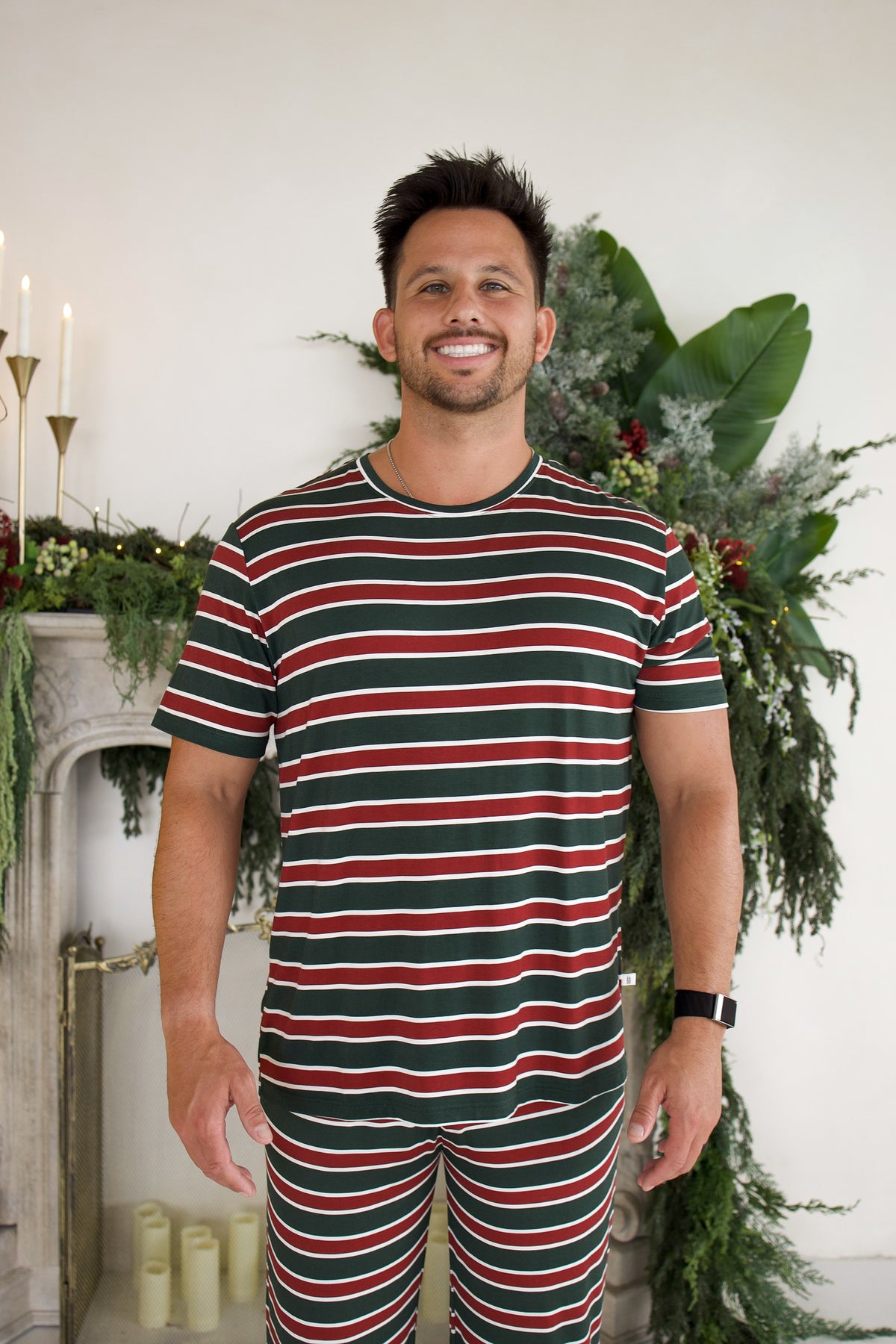 A man wearing a forever french baby Men’s Short Sleeve Pajamas | Holiday Stripe set featuring short sleeves and horizontal red, green, and white stripes.