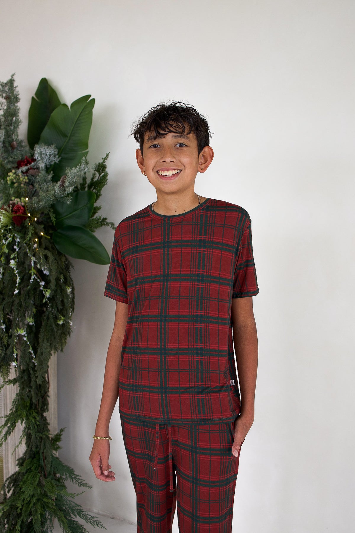 A smiling boy wearing a Youth Straight Leg Bamboo Pajamas | Christmas Plaid set with a red and green plaid pattern.