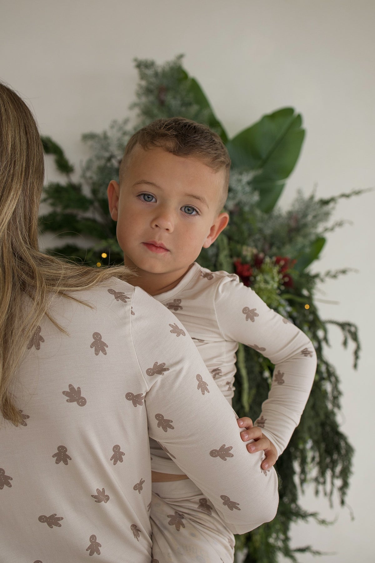 A woman holds a toddler, both wearing matching Bamboo Two Piece Pajamas | Gingersnap with a gingerbread man print.