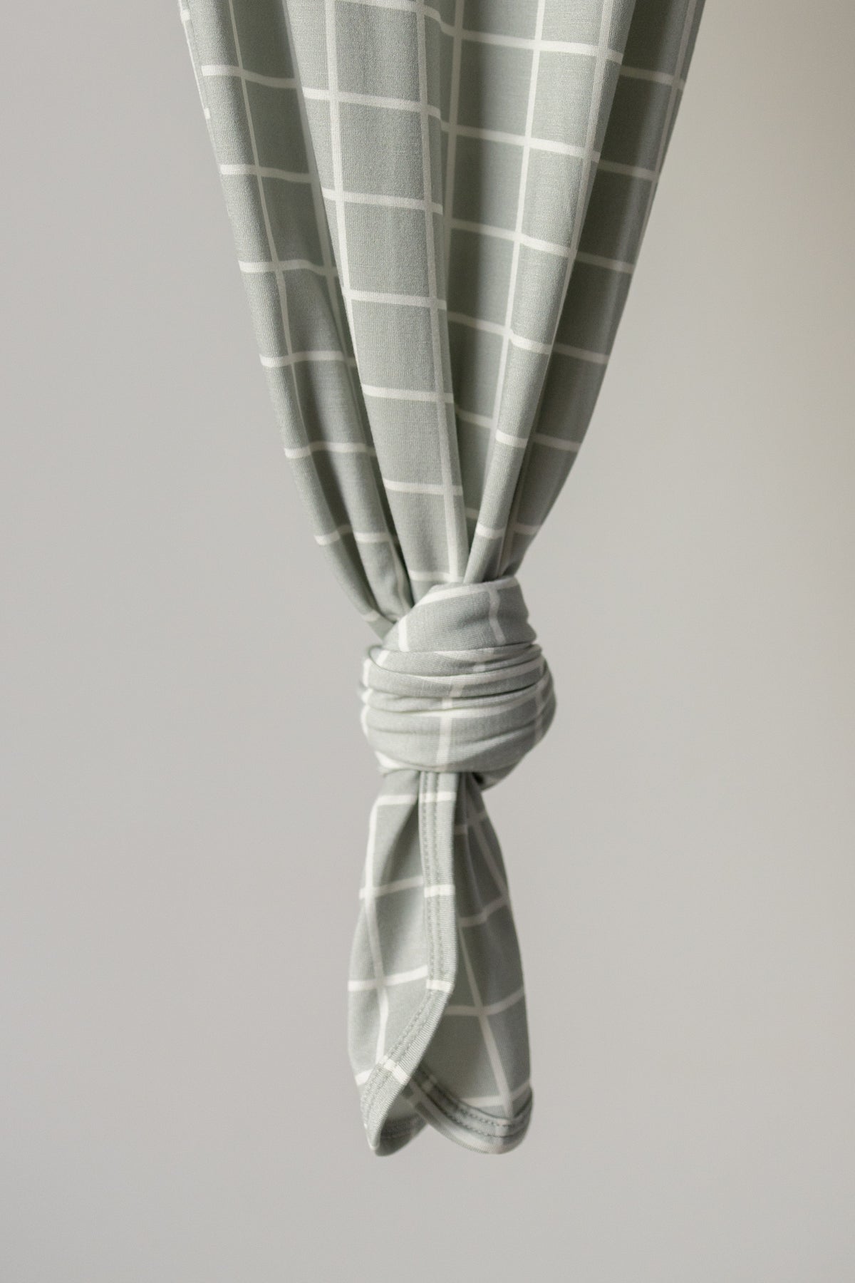 The Bamboo Knotted Gown | Foggy Grid by forever french baby features a light gray bamboo fabric adorned with a white grid pattern, tied in a neat knot and draping softly against a plain background—a newborn essential that pairs comfort with modern style.