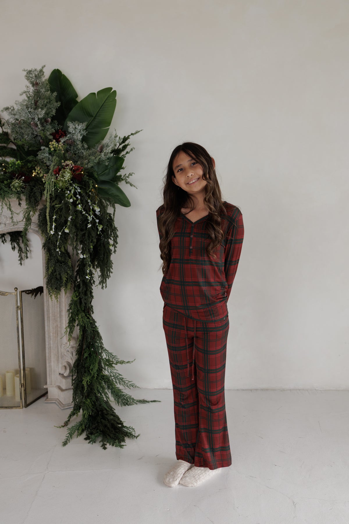 A smiling girl wearing Youth Flare Bamboo Pajamas | Christmas Plaid, consisting of a red and green plaid long-sleeve top and matching pants.