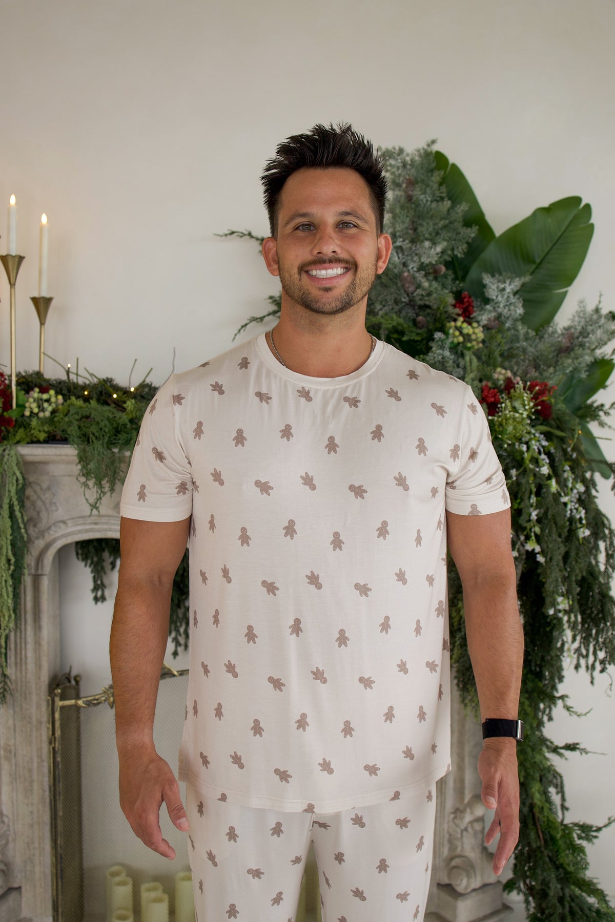 A man wearing a Men’s Short Sleeve Pajamas | Gingersnap set featuring a repeating gingerbread man pattern.
