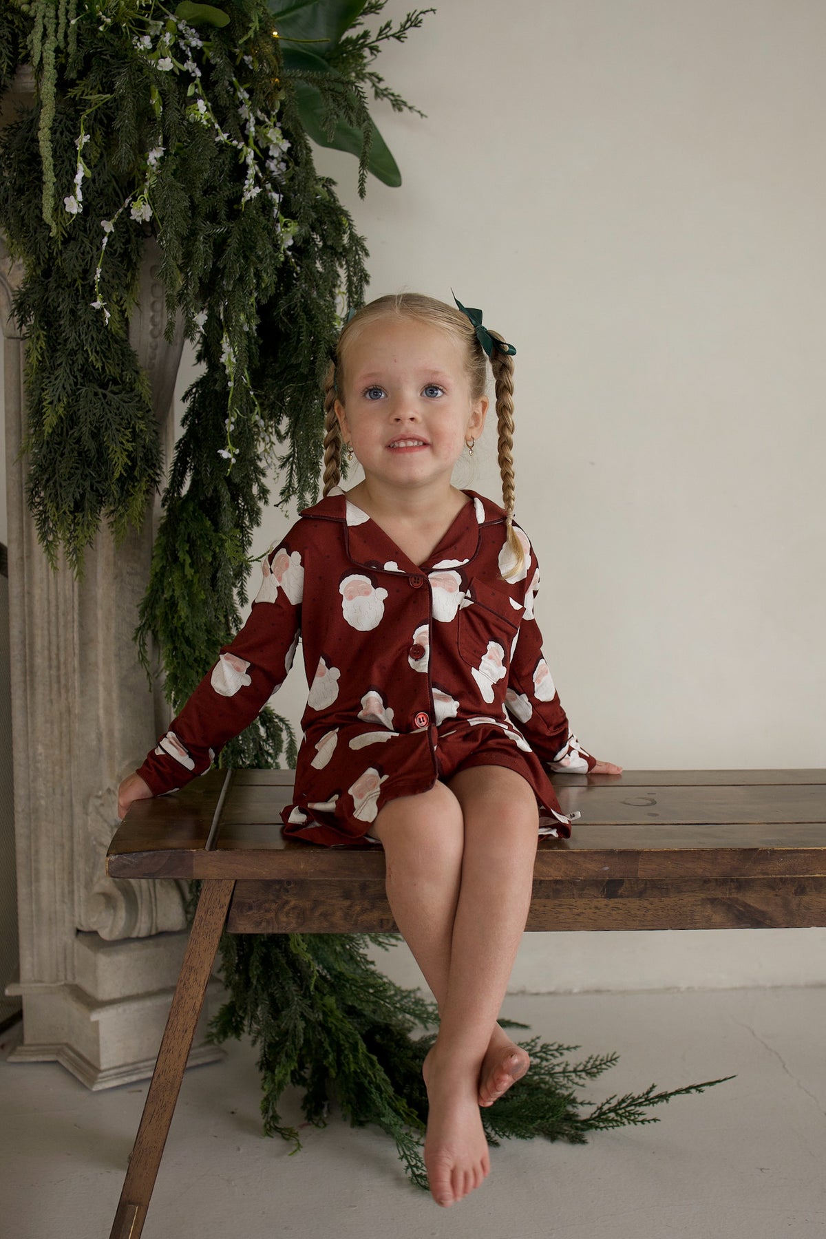A child wearing a long-sleeved, button-down Bamboo Sleeping Dress | Vintage Santa with a maroon background and a repeating vintage Santa Claus print.