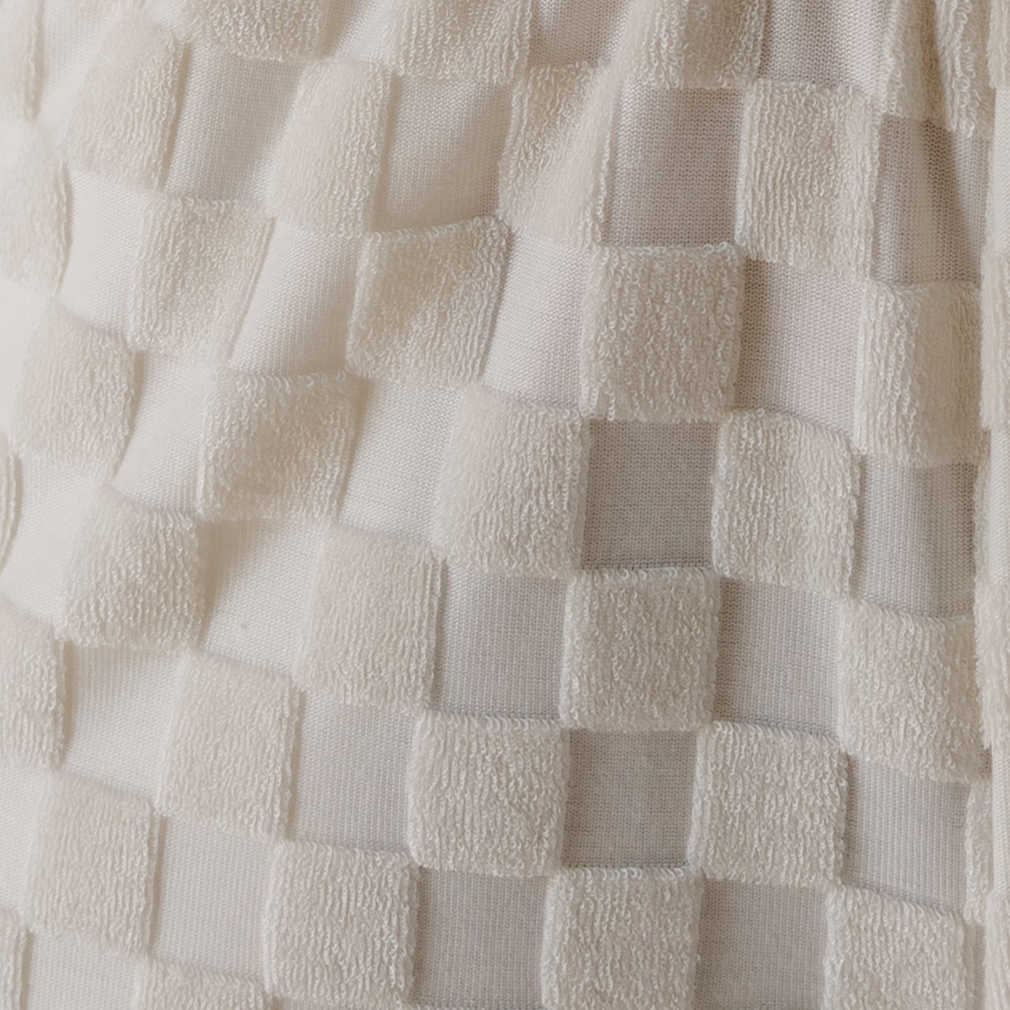 Close-up of a textured fabric with a cream checkerboard pattern, featuring alternating smooth and terry cloth squares on the forever french baby Women's Terry Short Set in Coconut Milk—ideal for comfortable loungewear.