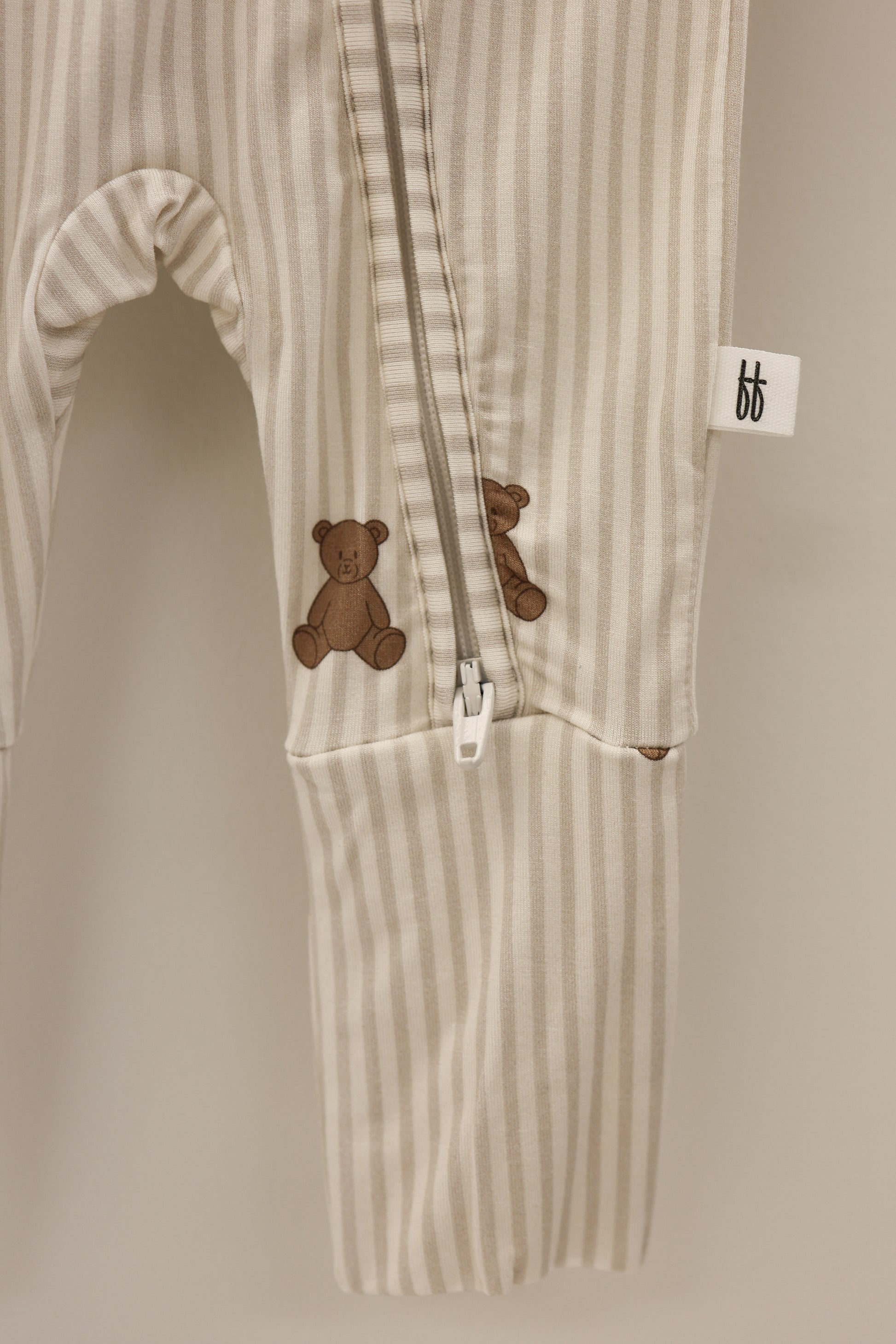 The forever french baby Bamboo Zip Pajamas | Teddy feature cream and beige stripes, a footed one-piece zip design, two small brown teddy bear accents on the leg, and a white "bf" tag on the side seam.