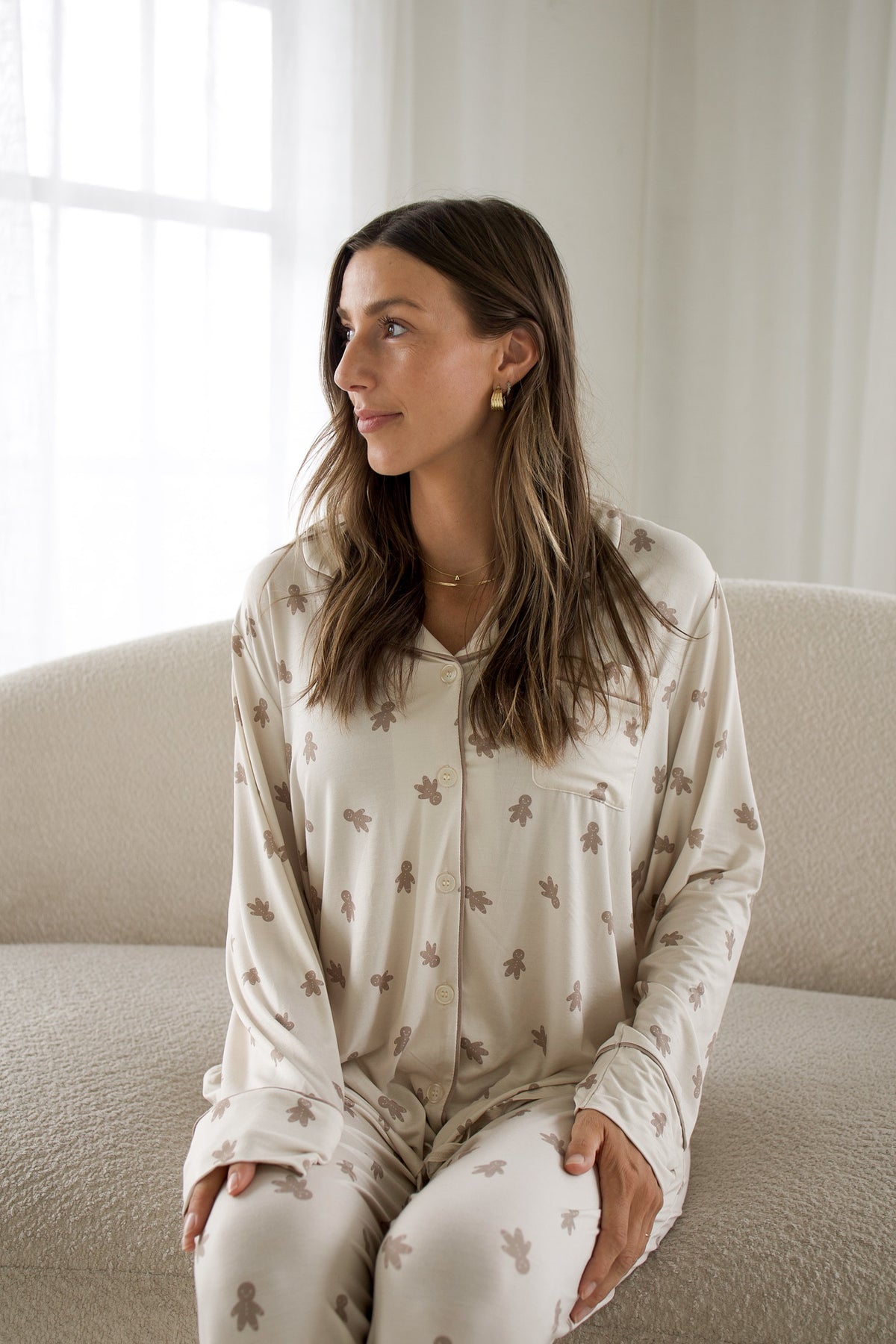 A woman wearing a Women’s Bamboo Button Up Lounge Set | Gingersnap in tan, featuring a long-sleeved button-down top and wide-leg lounge pants patterned with small brown gingerbread men.