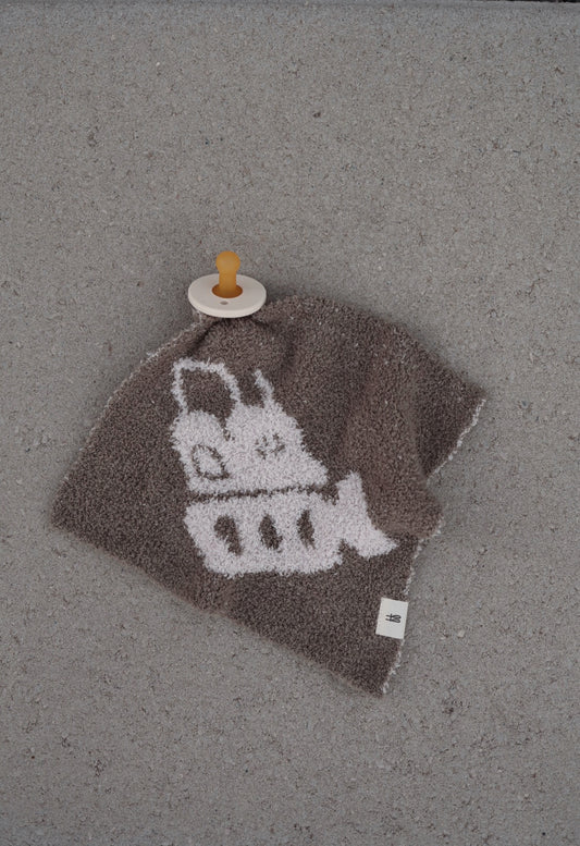 A brown "Lovey | Bulldozer" by forever french baby featuring a white cartoon bulldozer design rests on a gray surface, with a beige pacifier with brown nipple attached to one corner.