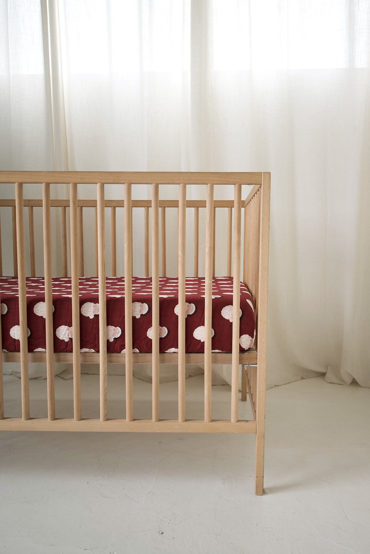 Wooden crib featuring a maroon Muslin Crib Sheet | Vintage Santa with a repeating vintage Santa Claus pattern.