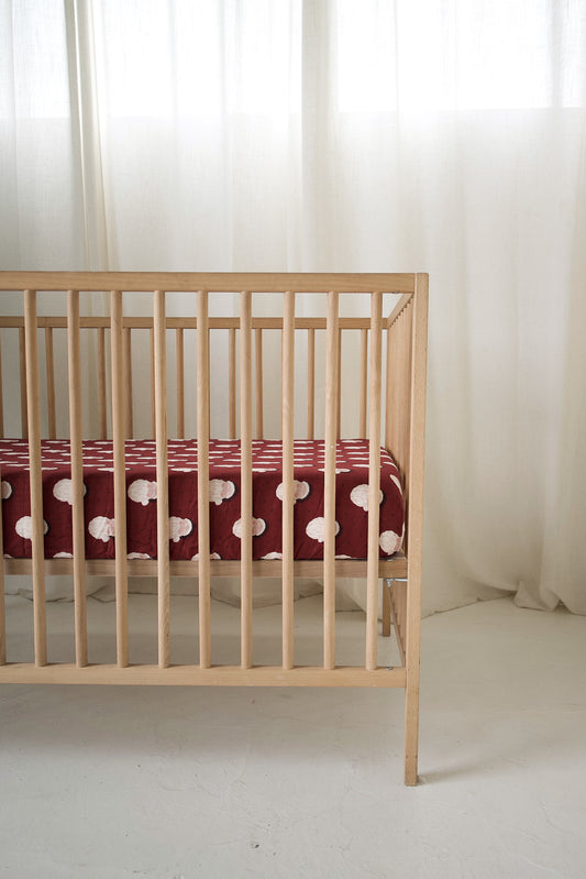Wooden crib featuring a maroon Muslin Crib Sheet | Vintage Santa with a repeating vintage Santa Claus pattern.