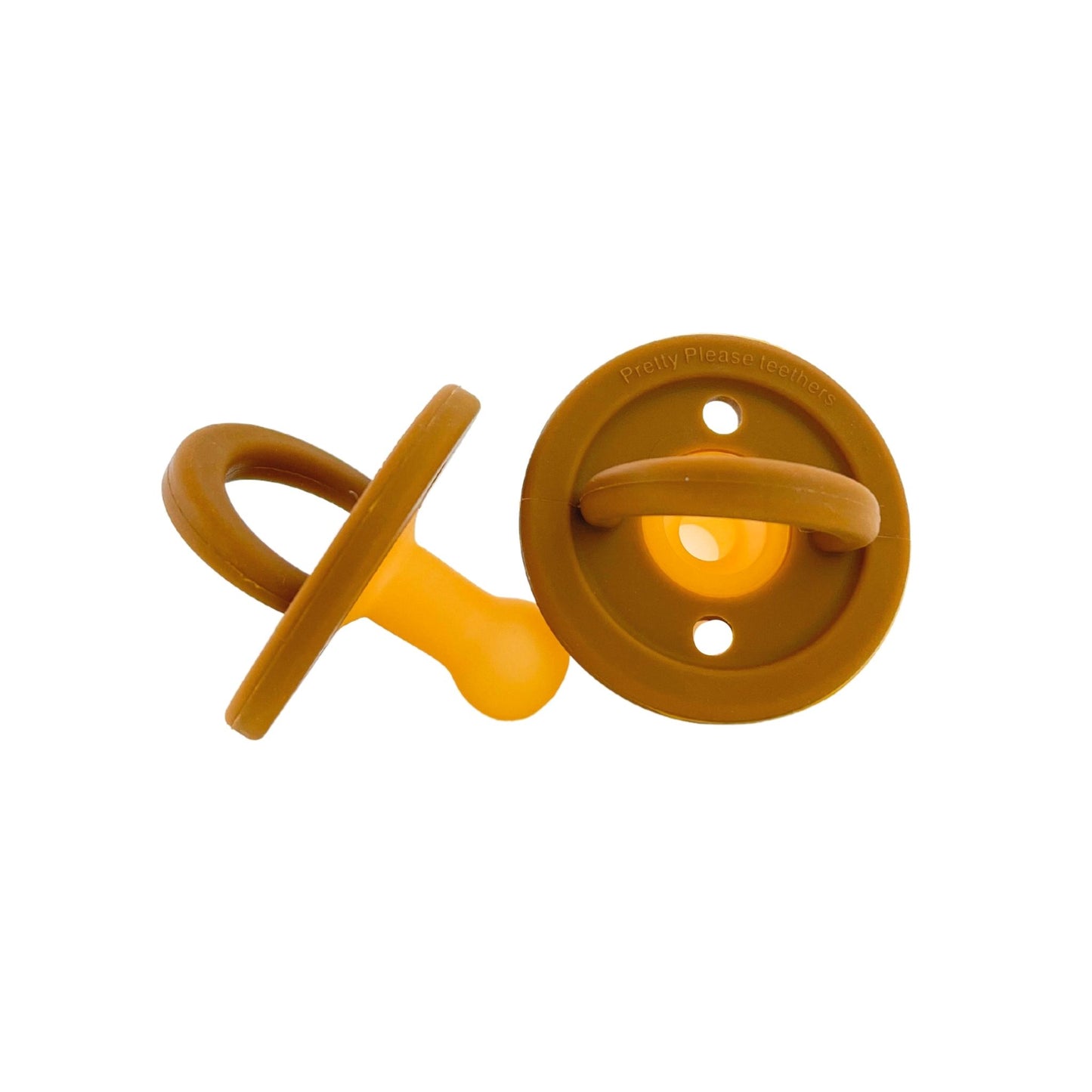 Two caramel-colored baby essentials, these Modern Pacifiers by forever french baby boast a simple, classic design with a round shield and looped handle. One stands upright while the other rests on its side. The yellow silicone nipple provides comfort and style against a clean white background.